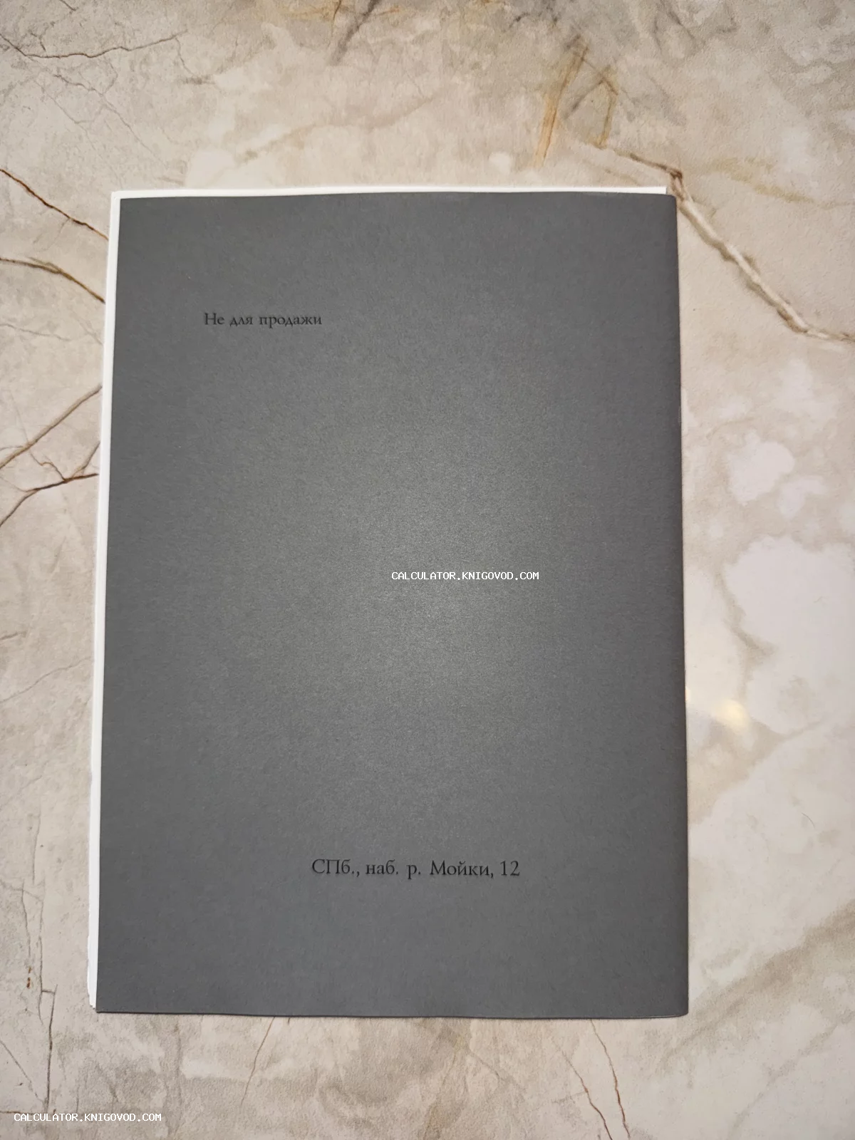 Темно-серая обложка брошюры с минималистичным текстом на русском языке, лежащая на мраморной поверхности.