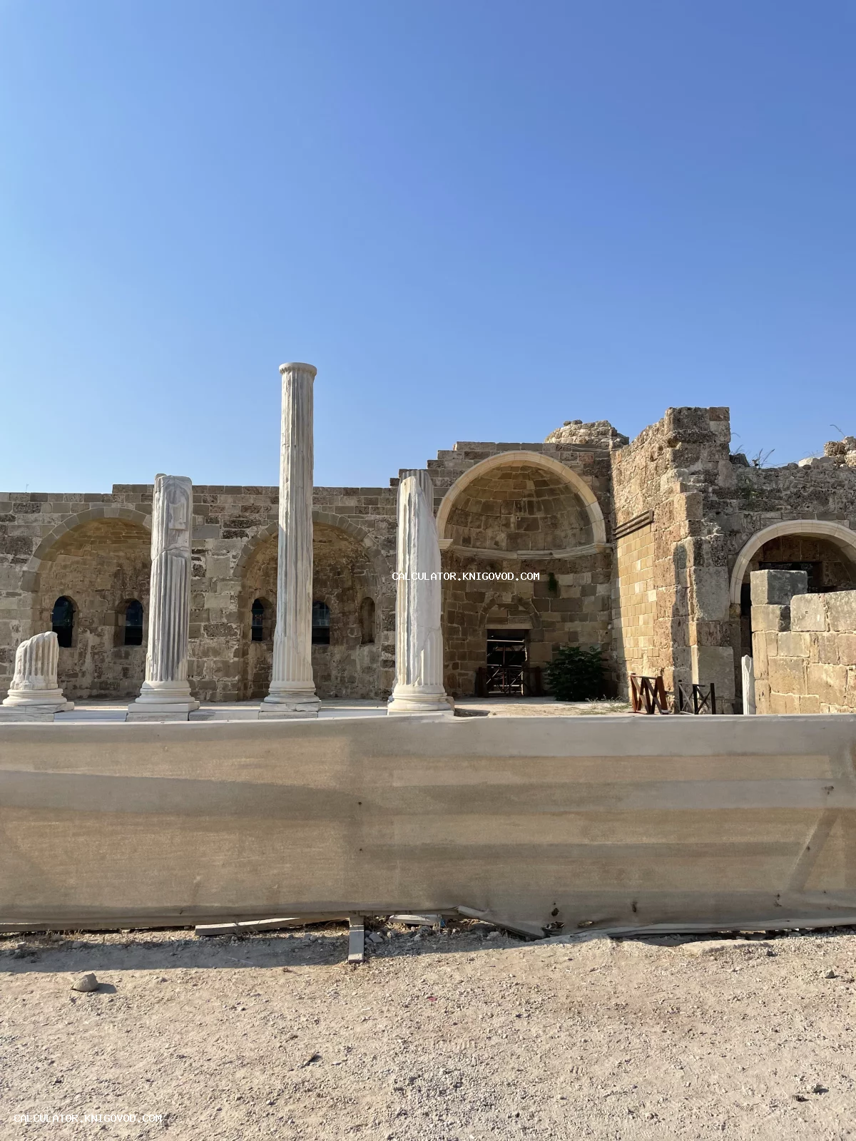 Вид на древние каменные арки и белые мраморные колонны античного храма под ясным небом.