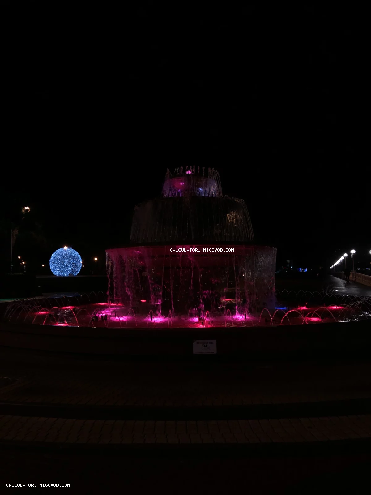 Многоярусный городской фонтан ночью с яркой розовой и красной подсветкой воды.