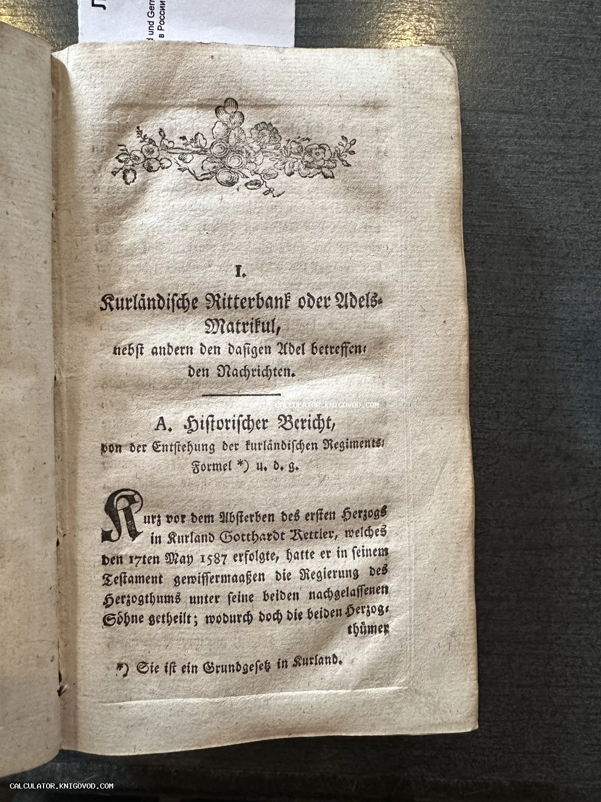 Разворот антикварной книги с готическим шрифтом на немецком языке, украшенный цветочной виньеткой сверху. Текст посвящен Курляндскому дворянскому матрикулу.