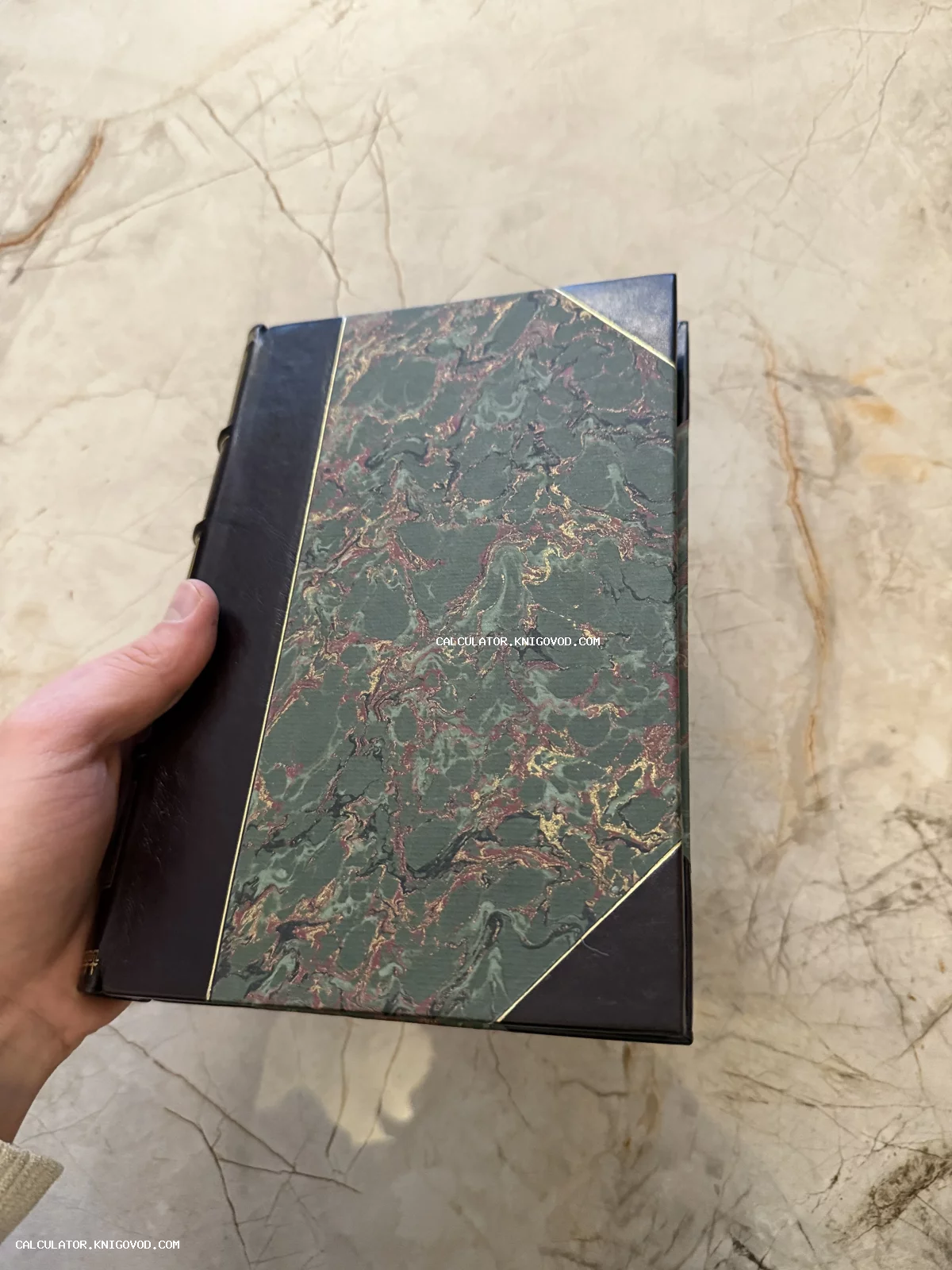 Старинная книга с темно-коричневым кожаным корешком и обложкой из зеленой мраморной бумаги на мраморном фоне