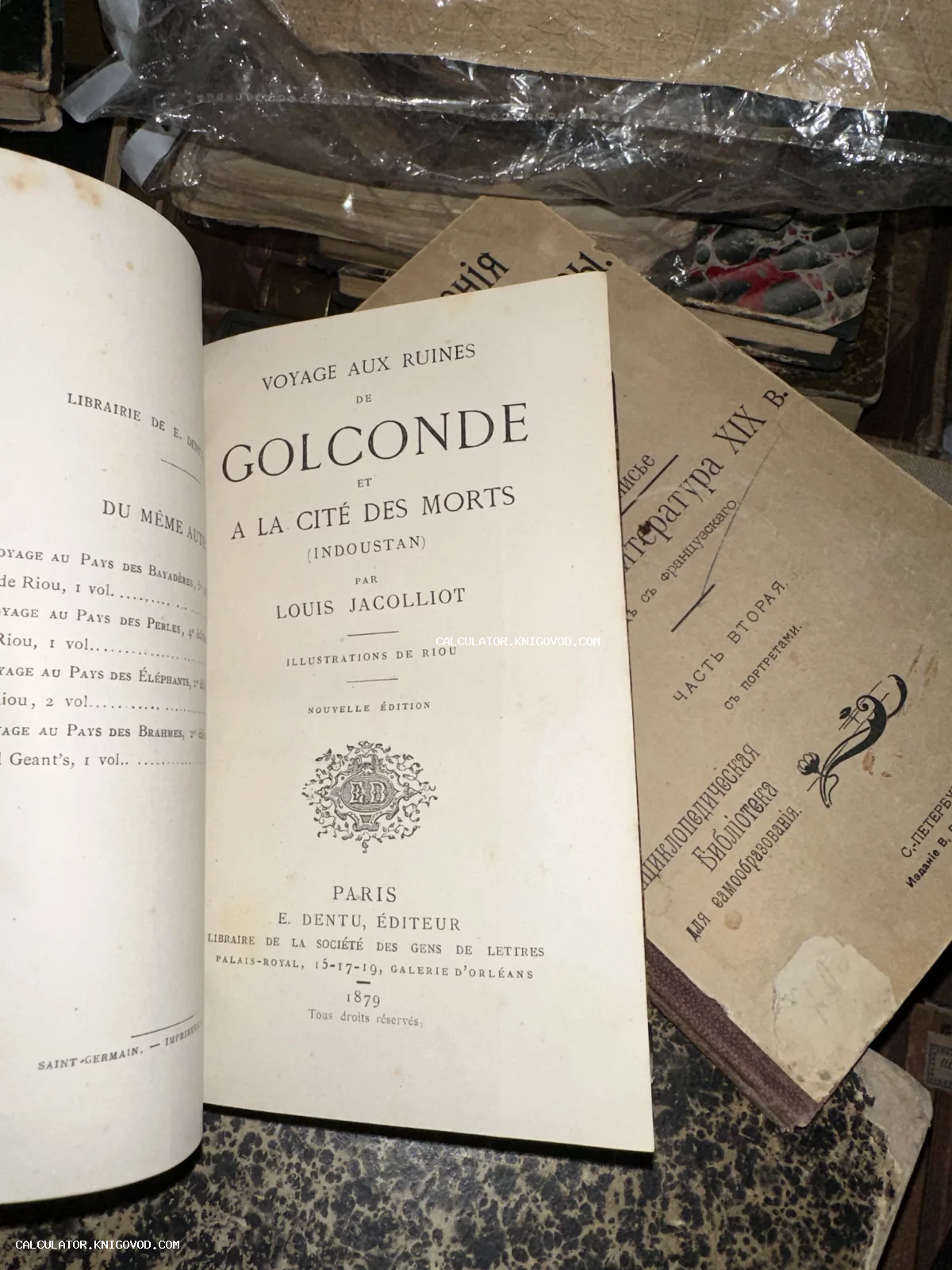Разворот старинной книги на французском языке с заголовком Voyage aux ruines de Golconde, 1879 год, на фоне других антикварных томов.