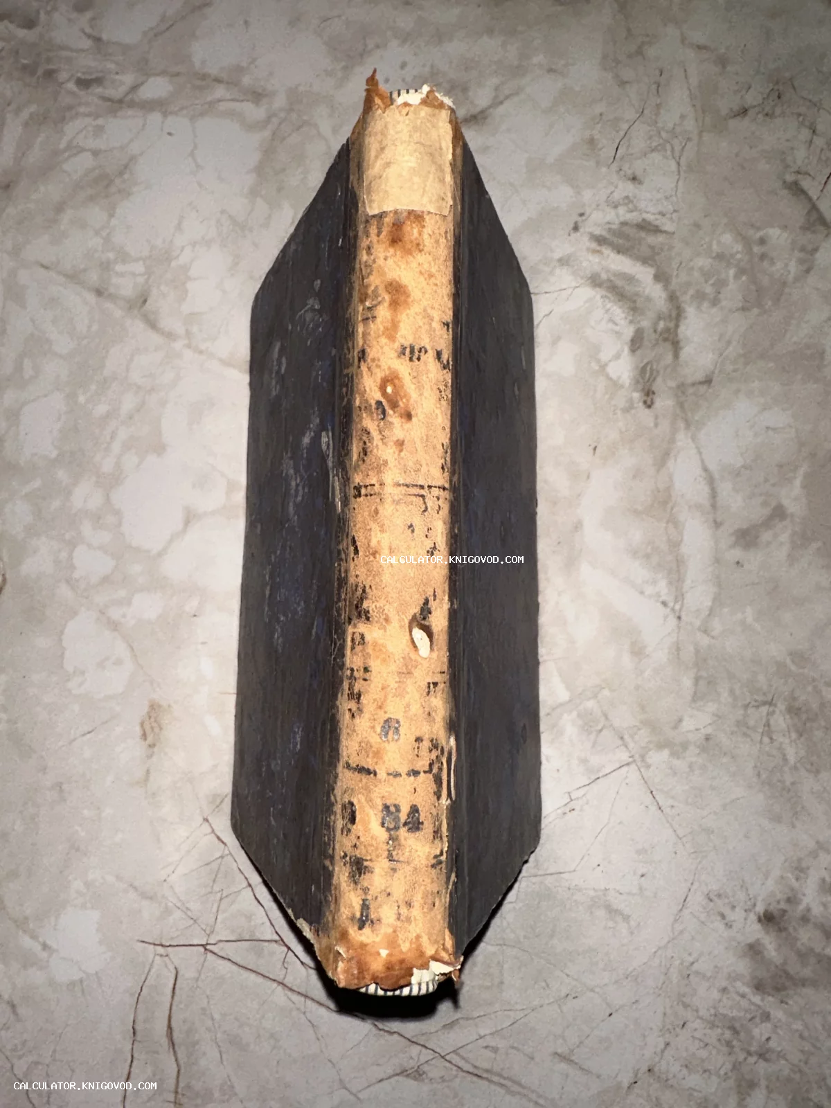 Вид сверху на старинную книгу с потертым желтоватым корешком и темными обложками на мраморном фоне.