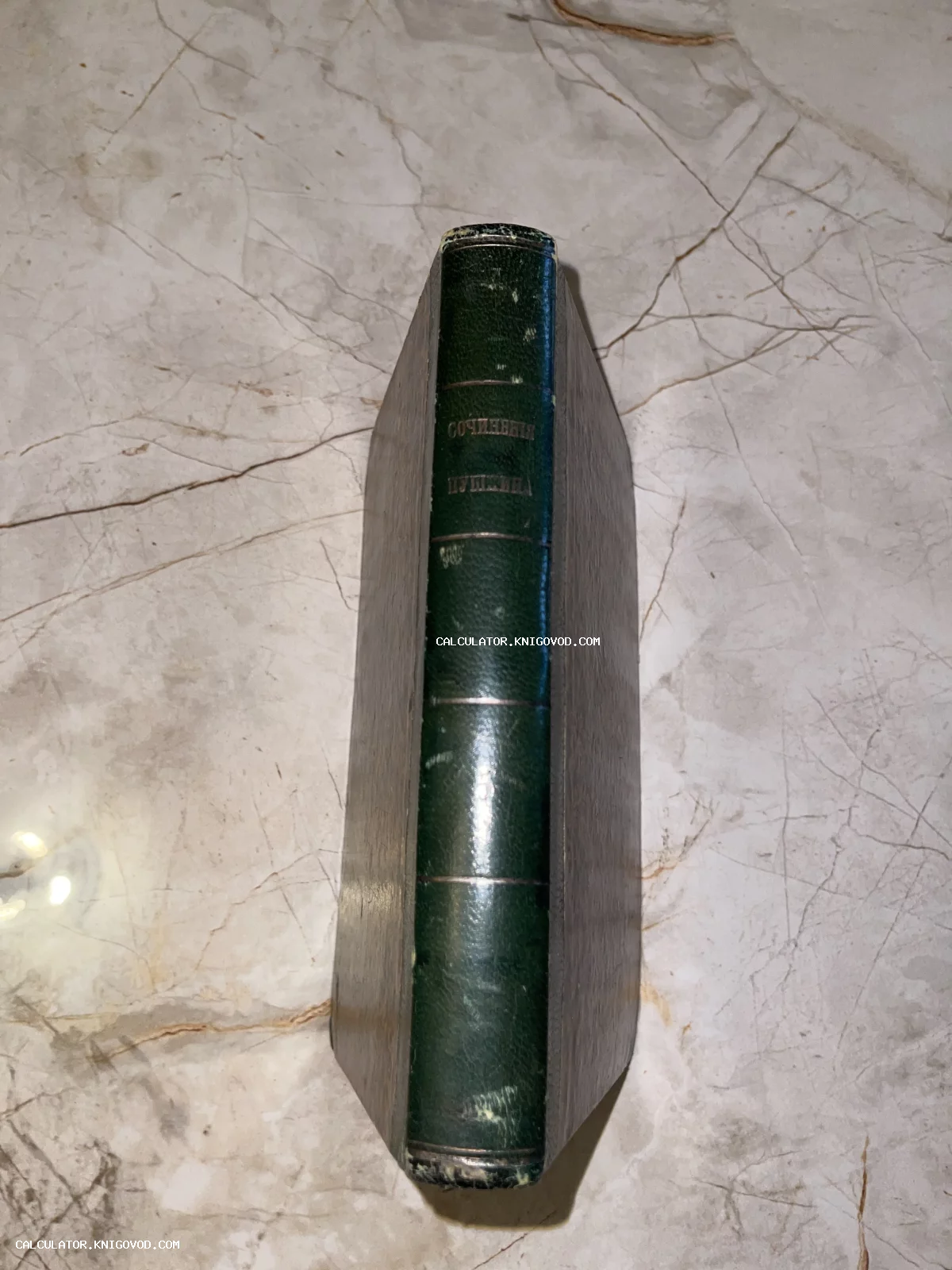 Корешок старинной книги с золотым тиснением «Сочинения Пушкина» в зеленом кожаном переплете на мраморном фоне.