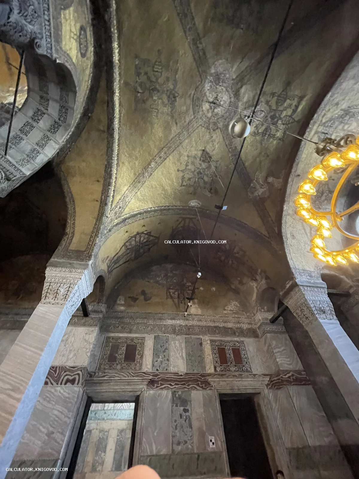 Вид на своды и потолок старинного храма с золотыми мозаиками, мраморными панелями на стенах и орнаментальной резьбой.