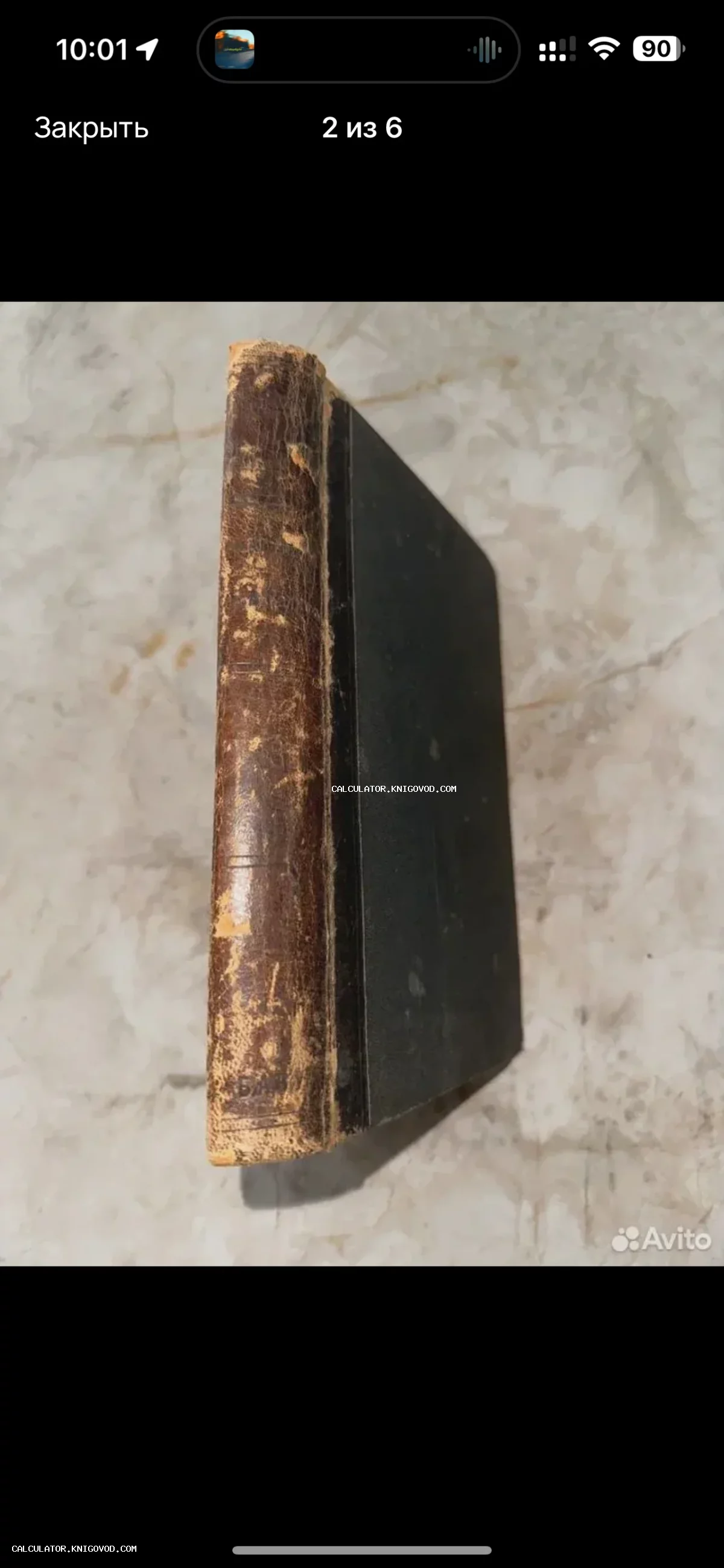 Вид на потертый кожаный корешок и темную обложку старинной антикварной книги на светлом фоне.