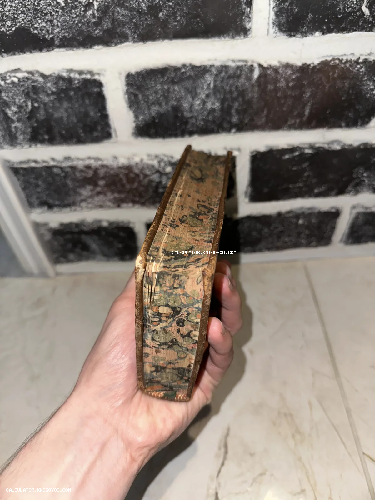 Старинная книга в руке, вид сверху на декоративный мраморный обрез и потертый кожаный переплет.