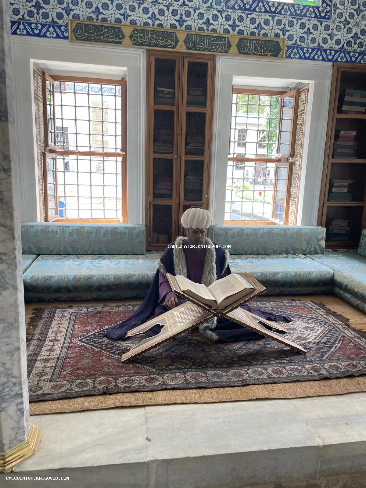 Фигура ученого в тюрбане, читающего древнюю книгу на резной подставке в османском интерьере с голубыми изразцами.