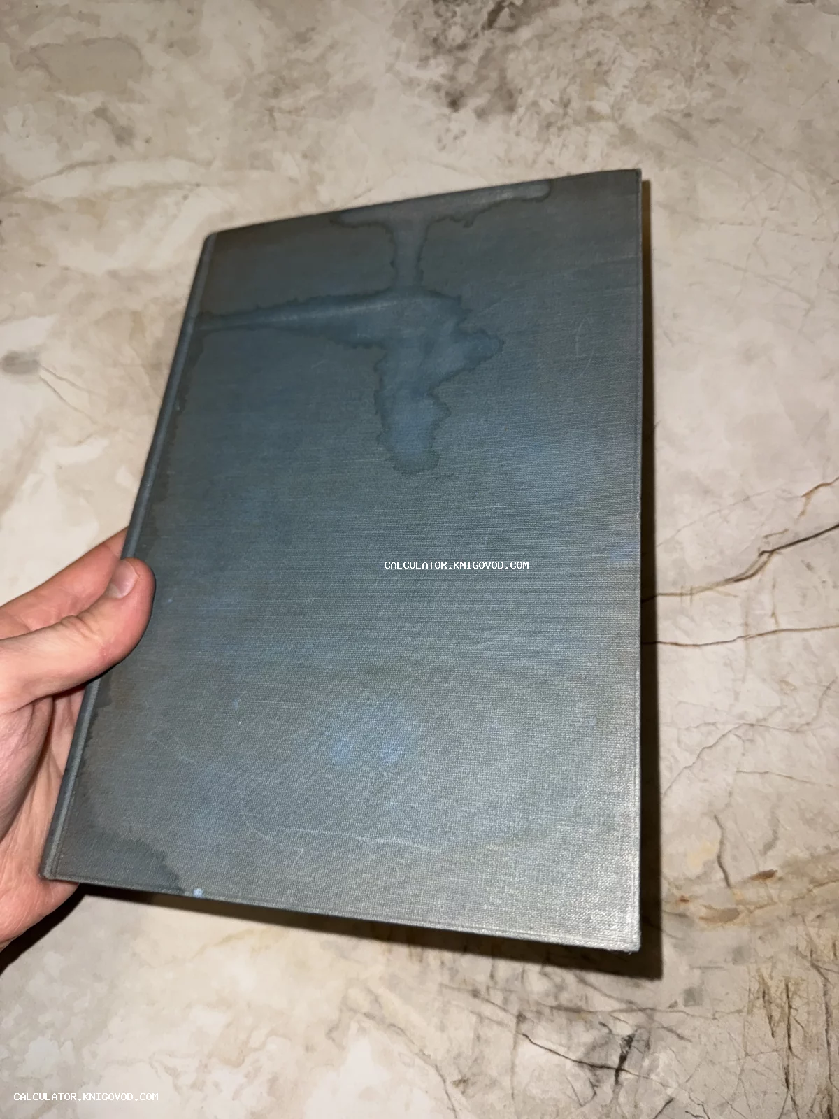 Старая книга в сером коленкоровом переплете с видимыми следами влаги на обложке.