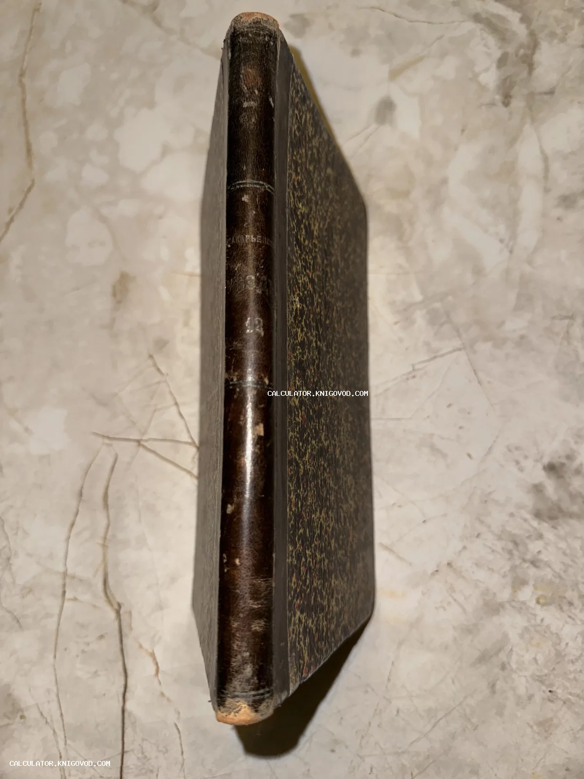 Старинная книга в полукожаном переплете с тиснением на корешке и обложкой из мраморной бумаги на светлом фоне