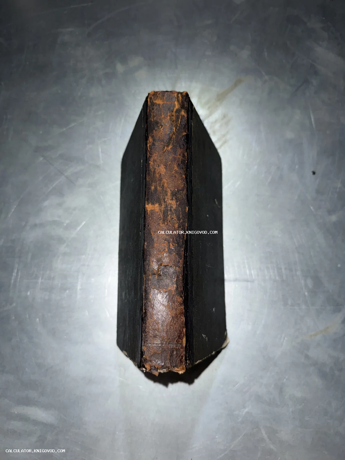 Вид сверху на изношенный корешок старинной книги из коричневой кожи и темные крышки переплета.