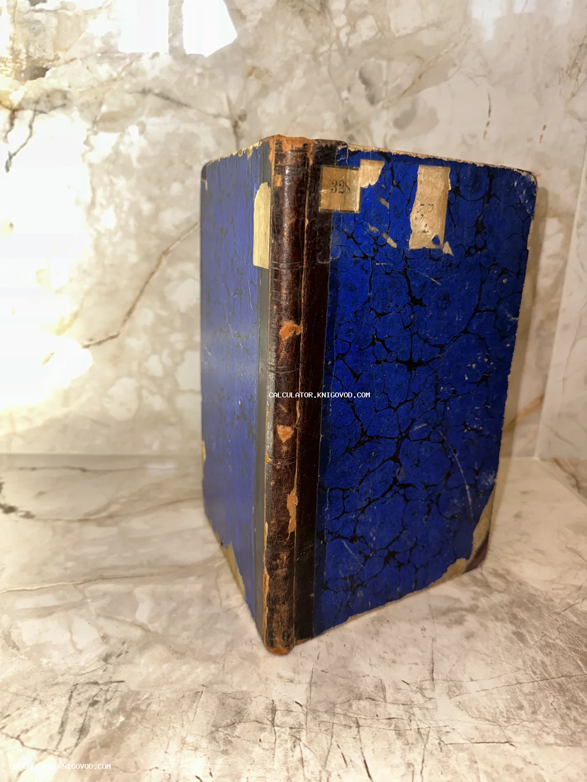 Старинная книга с синей мраморной обложкой и потертым кожаным корешком на мраморном фоне.