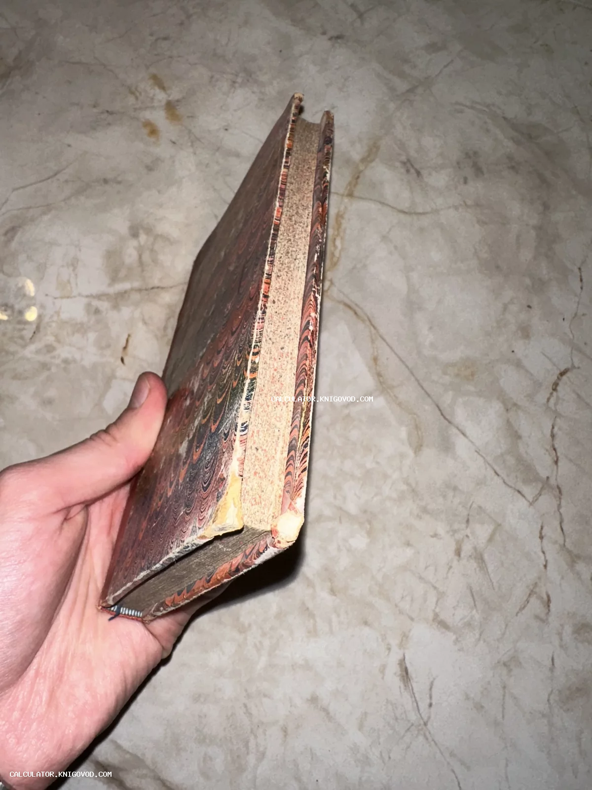 Антикварная книга с обложкой из мраморной бумаги ручной работы в руке коллекционера.