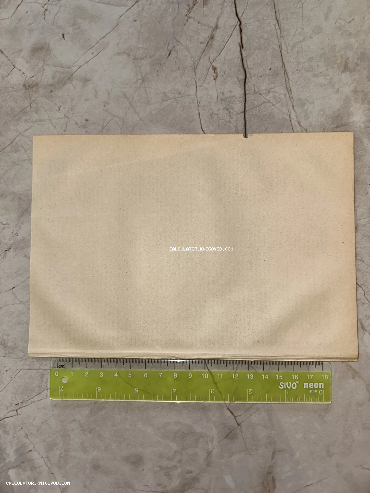 Пожелтевший антикварный лист бумаги на мраморной поверхности рядом с измерительной линейкой.