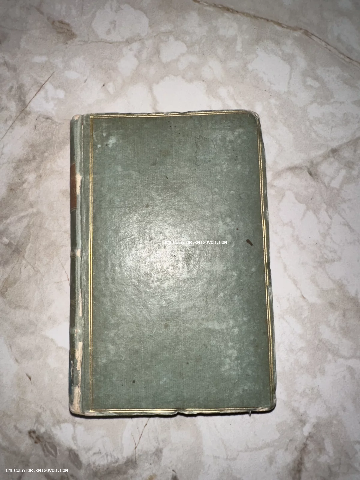 Антикварная книга в потертом зеленом переплете с тонкой золотой рамкой на обложке, вид сверху.