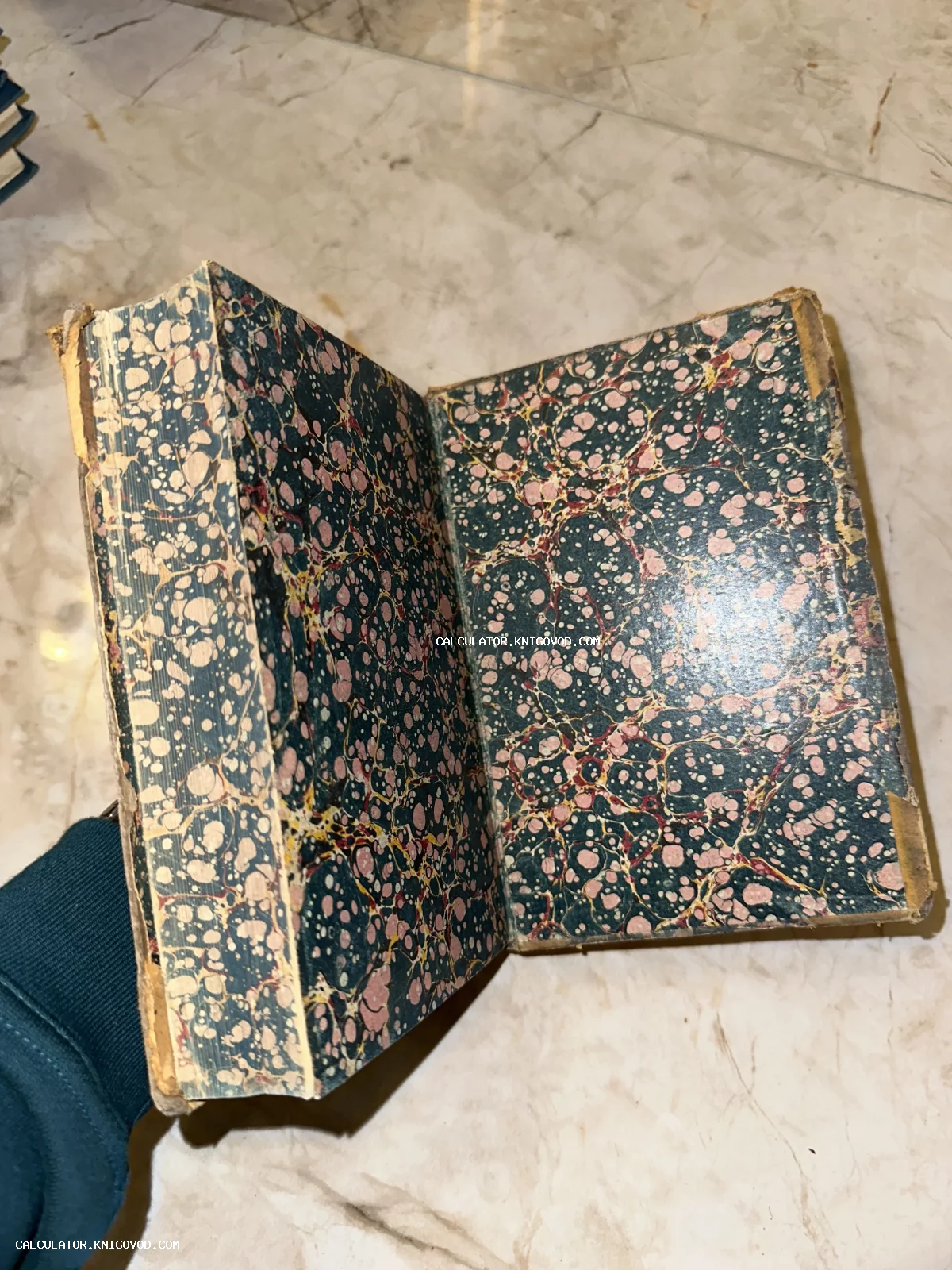 Раскрытая старинная книга, демонстрирующая узорчатую мраморную бумагу ручной работы на форзаце и потертый временем переплет.