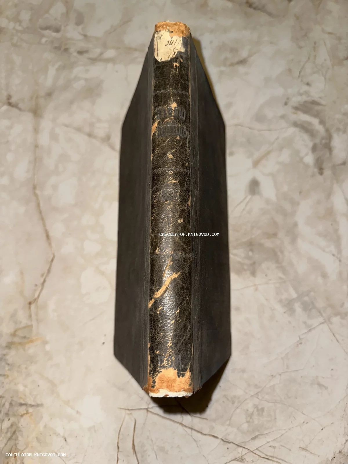 Вид сверху на потертый корешок старинной книги в темном кожаном переплете с остатками золотого тиснения.