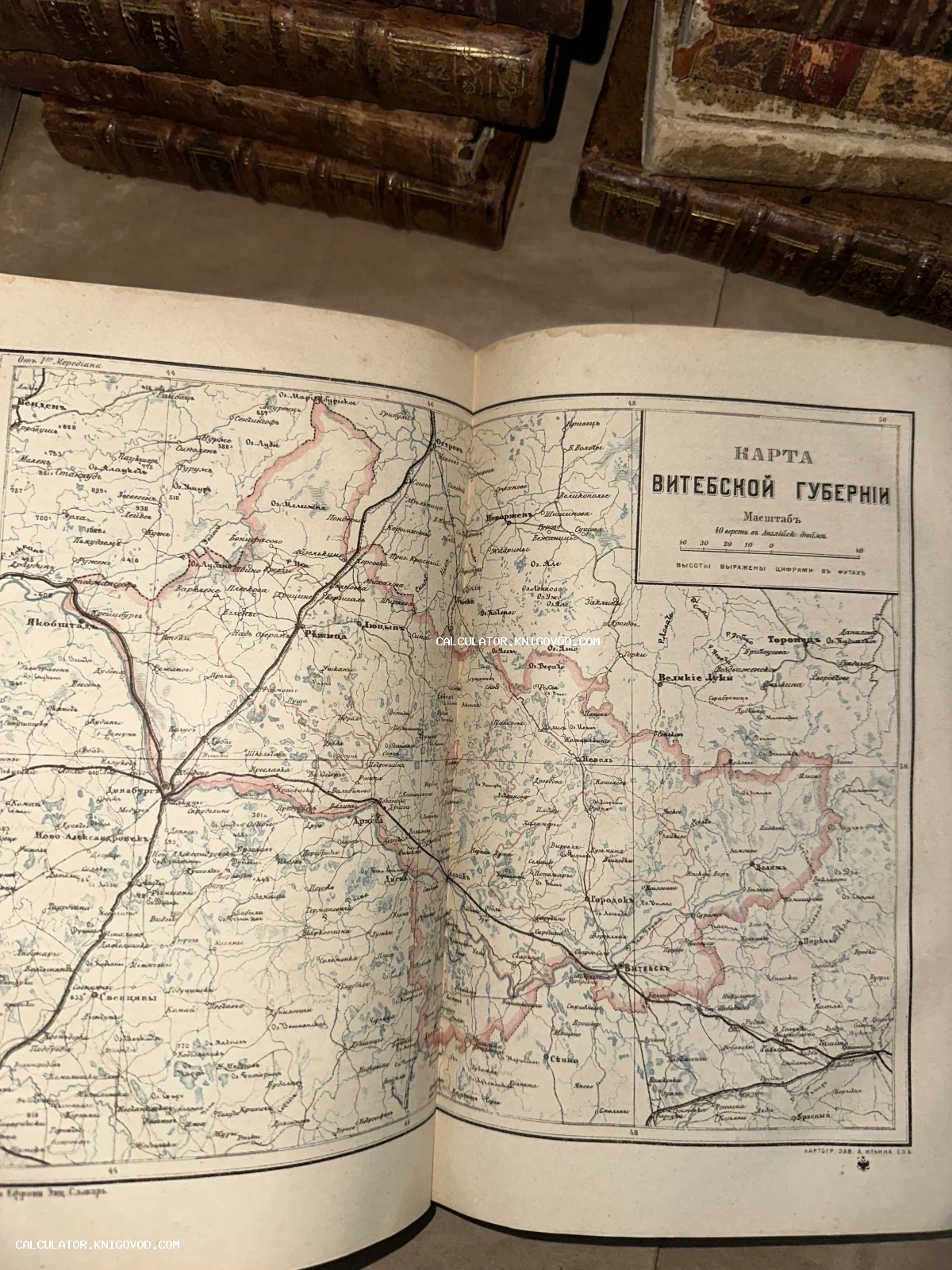 Разворот антикварного атласа с подробной картой Витебской губернии на фоне старых кожаных книг.