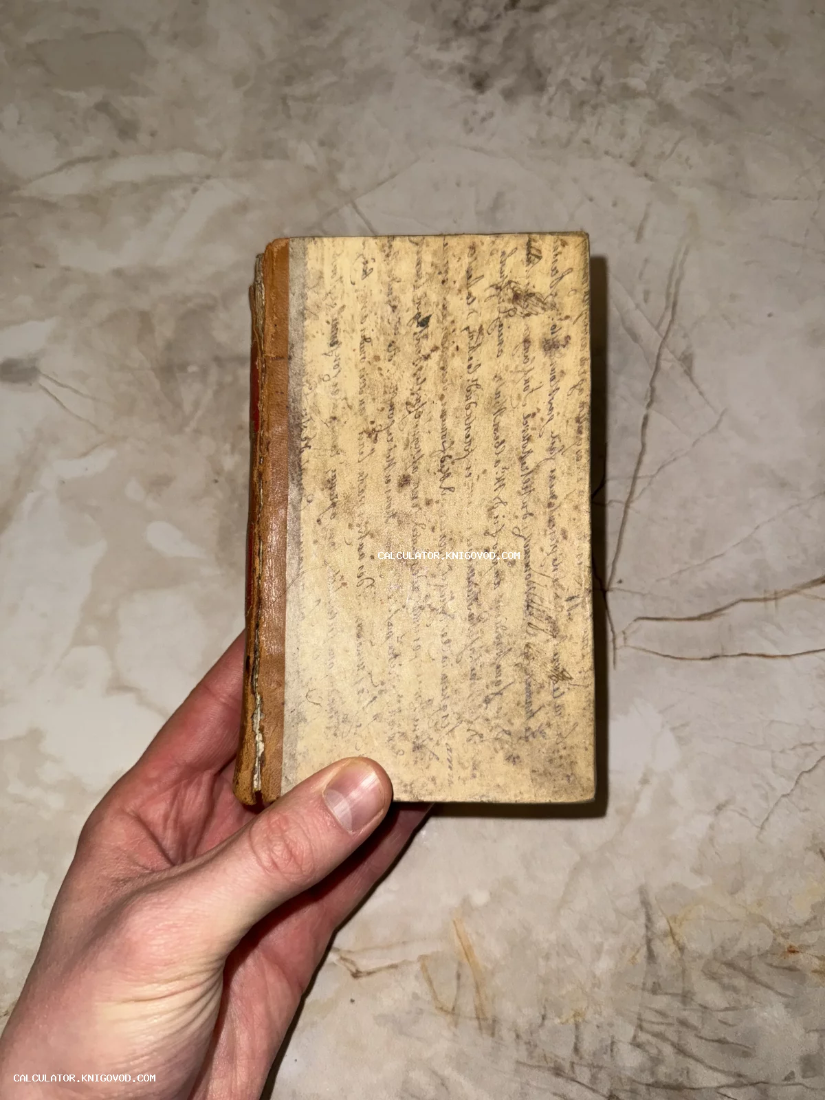 Старинная малоформатная книга с обложкой из фрагмента рукописи с каллиграфическим почерком в руке человека.