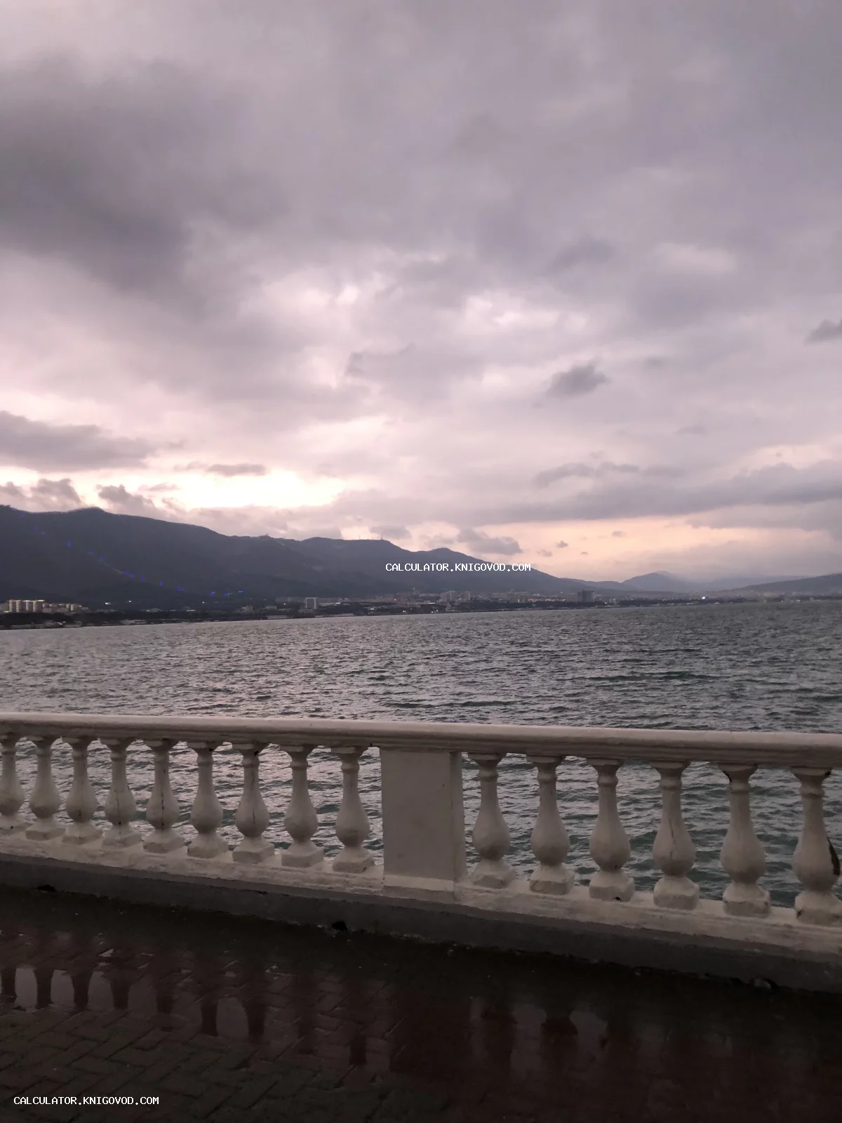 Классическая белая балюстрада на фоне морского залива и гор под пасмурным небом.