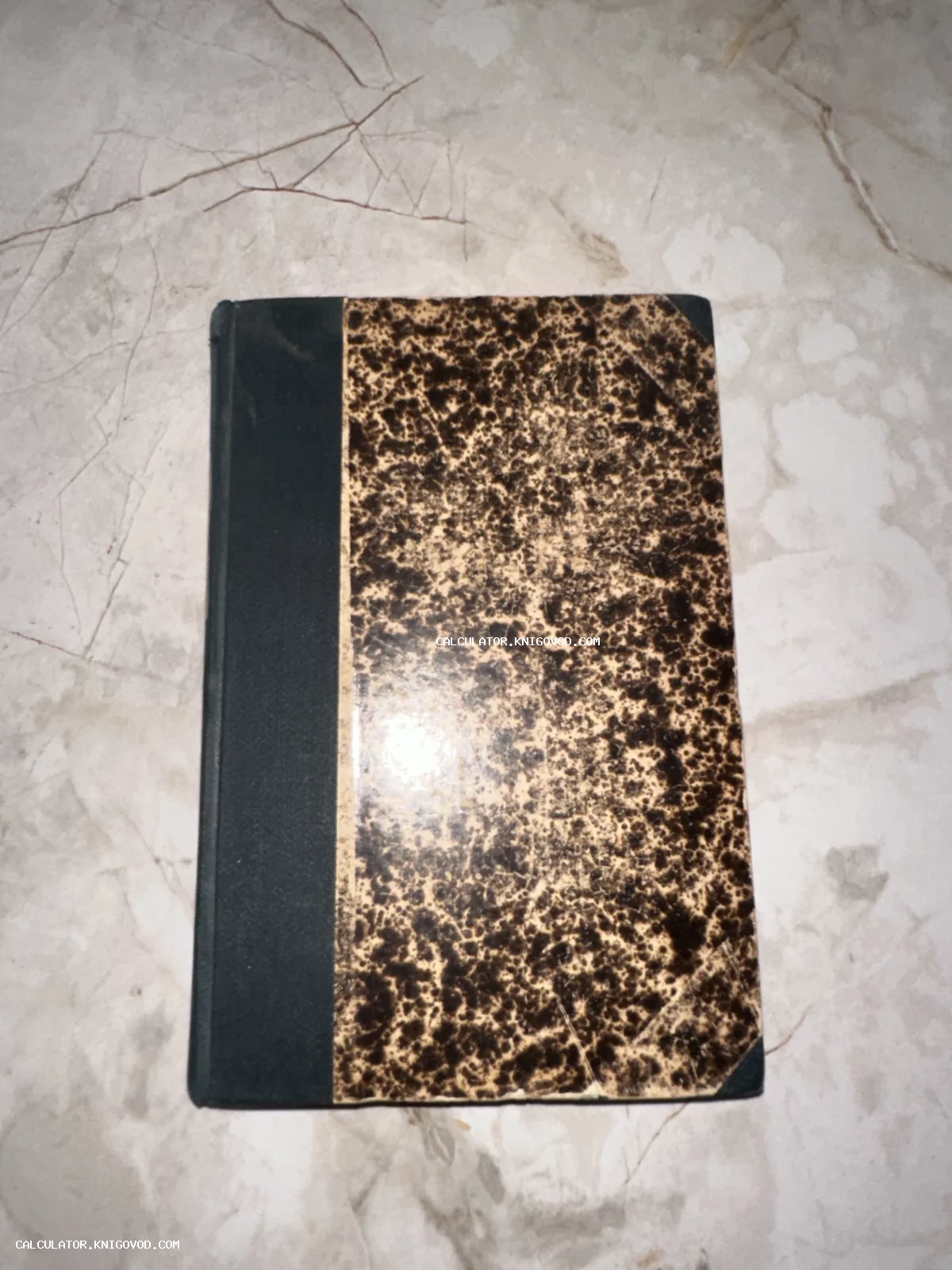 Старинная книга или блокнот с темным корешком и обложкой из мраморной бумаги коричневых оттенков на светлом фоне.