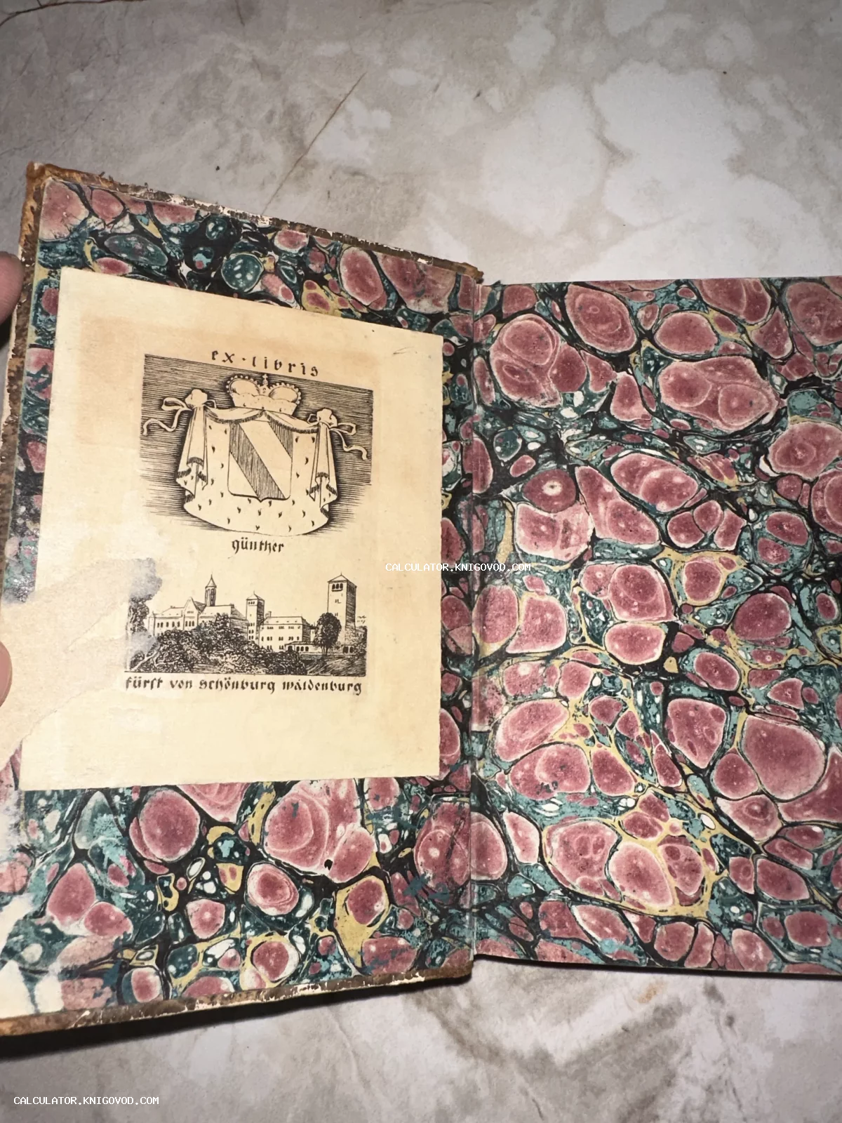 Внутренняя сторона переплета старинной книги с яркой мраморной бумагой и наклеенным гербовым экслибрисом князя Шёнбург-Вальденбурга.
