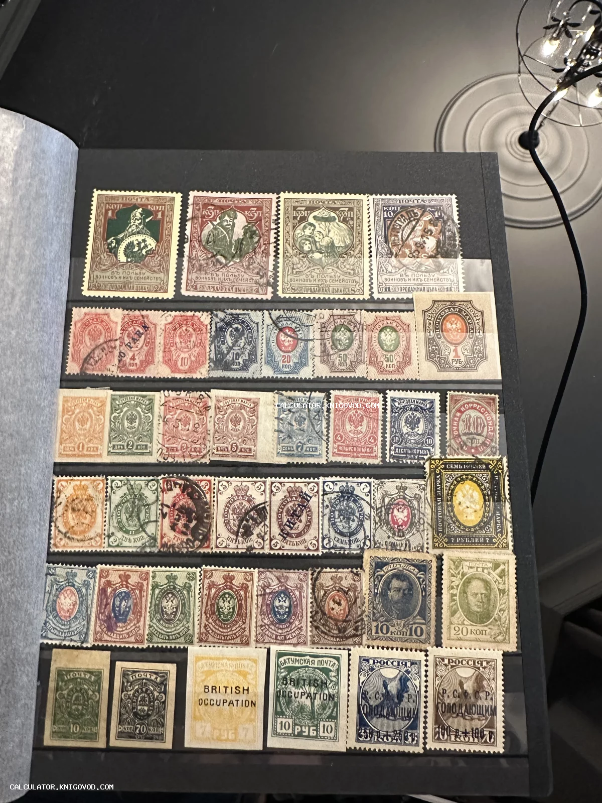 Страница черного филателистического кляссера с рядами антикварных почтовых марок начала XX века, включая имперские гербы и надпечатки британской оккупации.