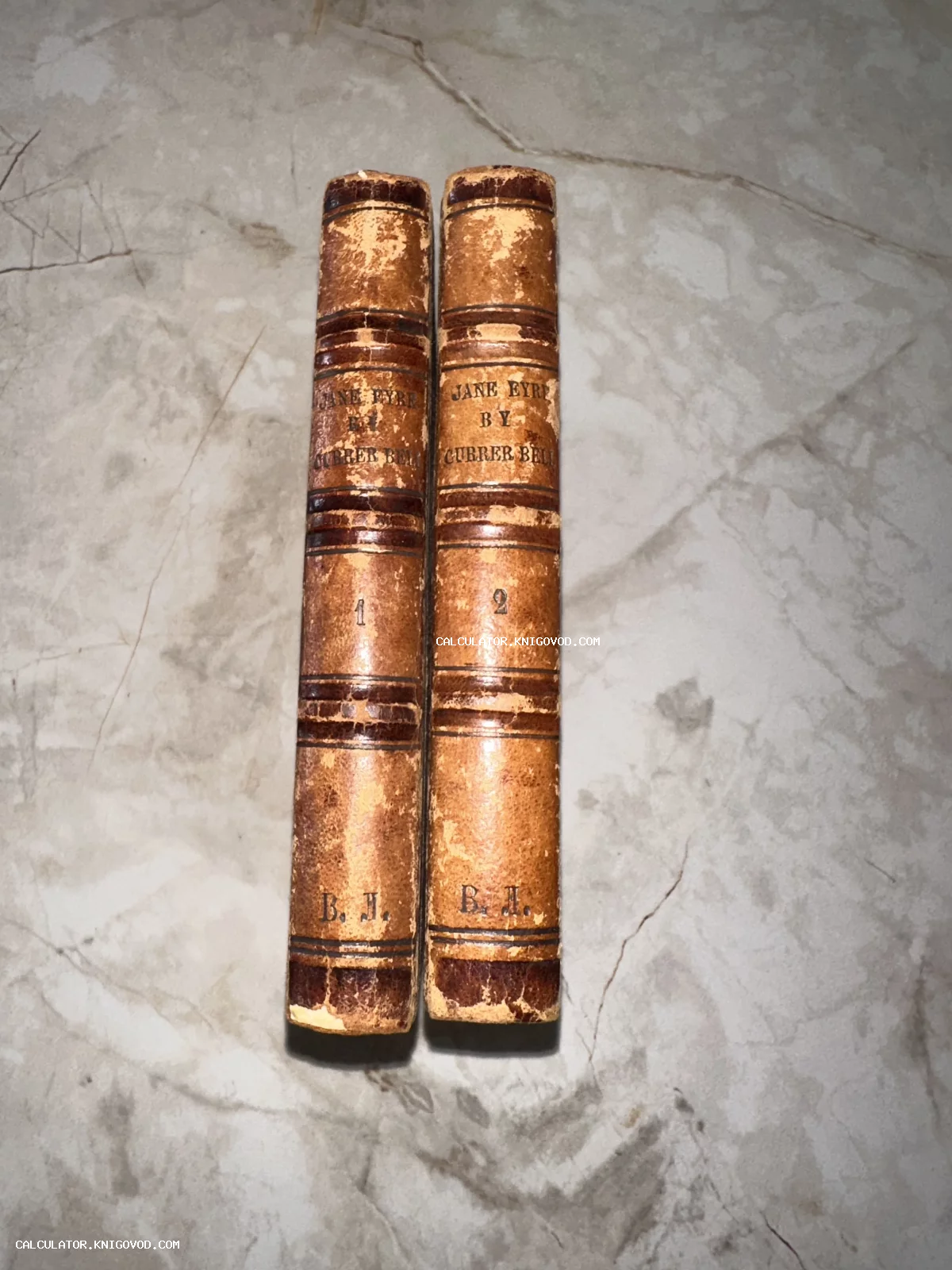 Корешки двух старинных книг в кожаном переплете с тиснением Jane Eyre by Currer Bell на мраморной поверхности.