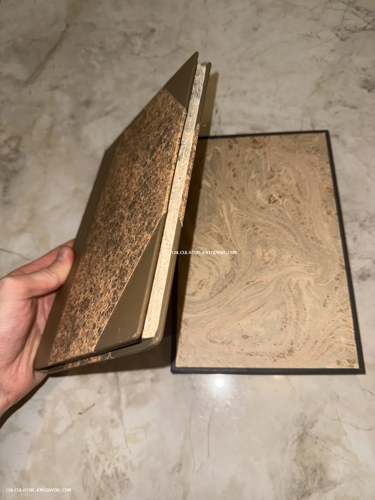 Старинная книга с обложкой из мраморной бумаги коричневого оттенка и кожаными уголками в руке.