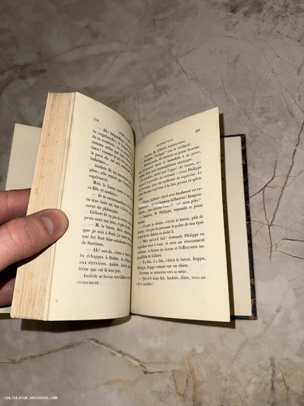 Раскрытая старинная книга на французском языке с пожелтевшими от времени страницами, которую придерживает рука.