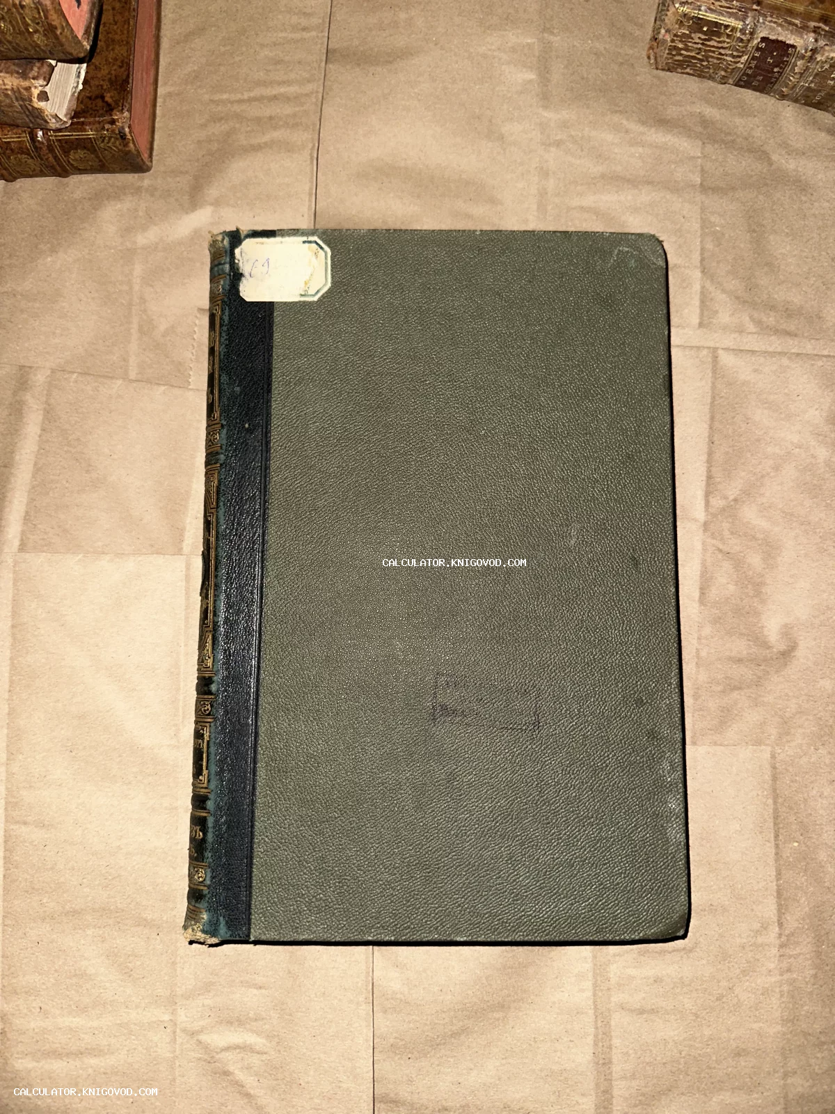 Вид сверху на антикварную книгу с зелеными фактурными крышками и темным кожаным корешком с золотым тиснением.