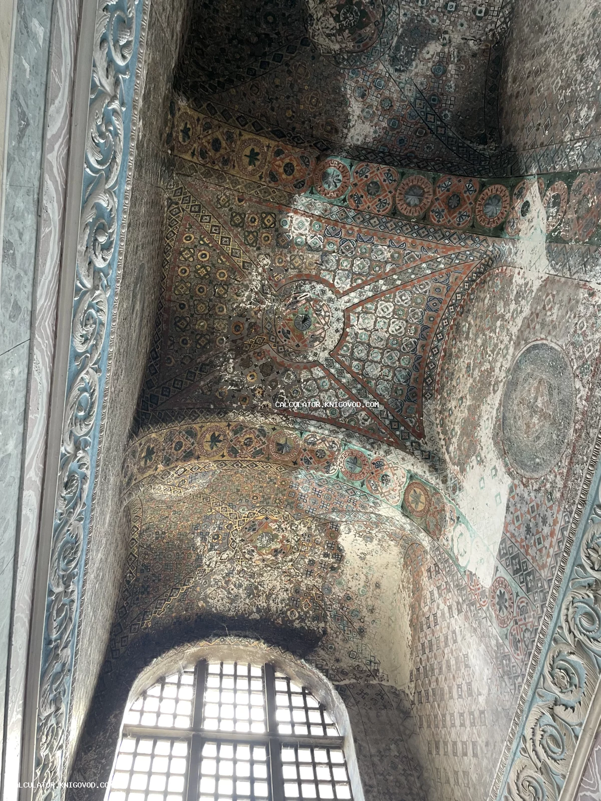 Старинная византийская мозаика на потолочных сводах с геометрическим орнаментом и арочное окно с решеткой.