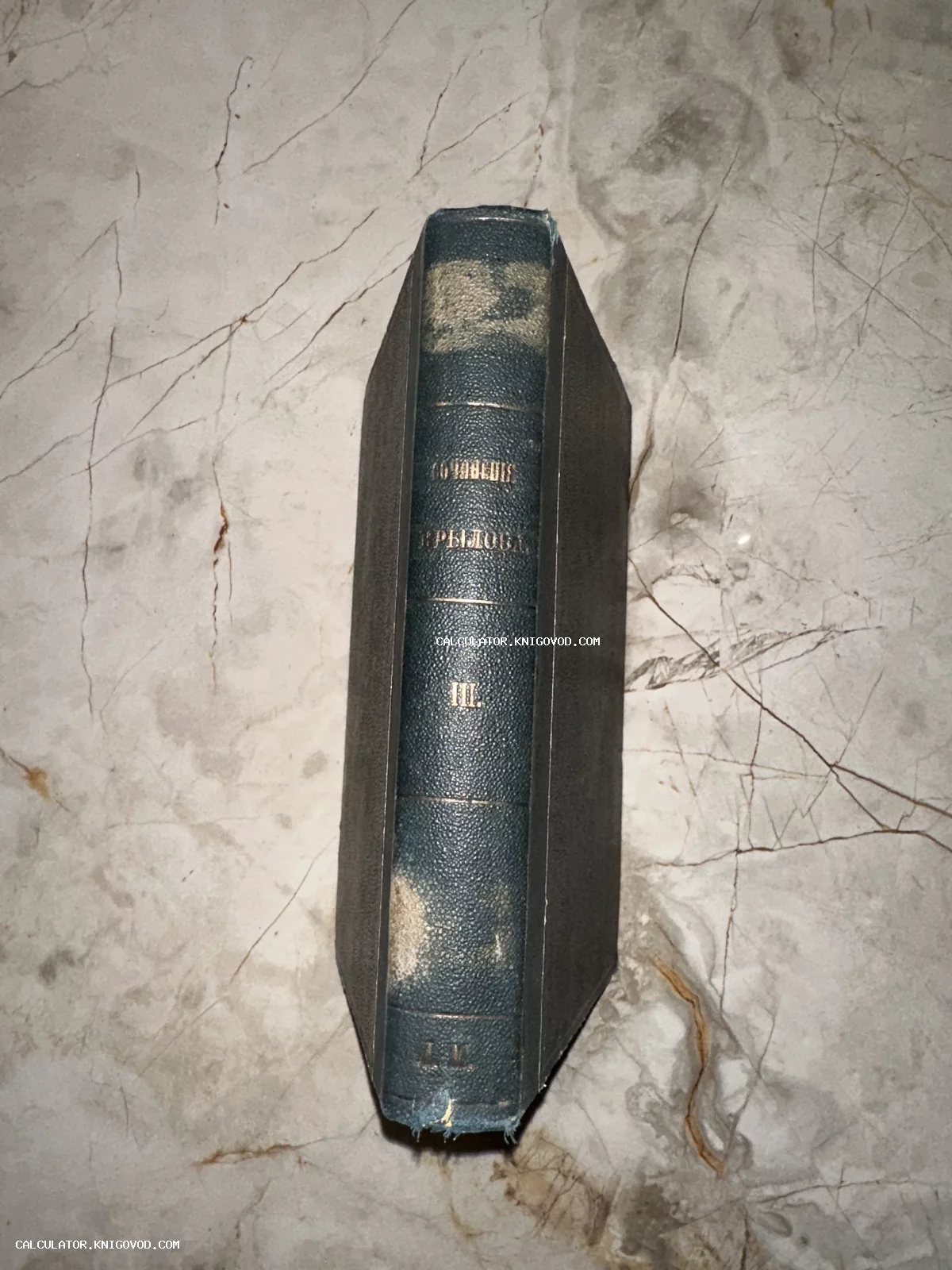 Корешок антикварной книги с золотым тиснением Сочинения Крылова на мраморном фоне