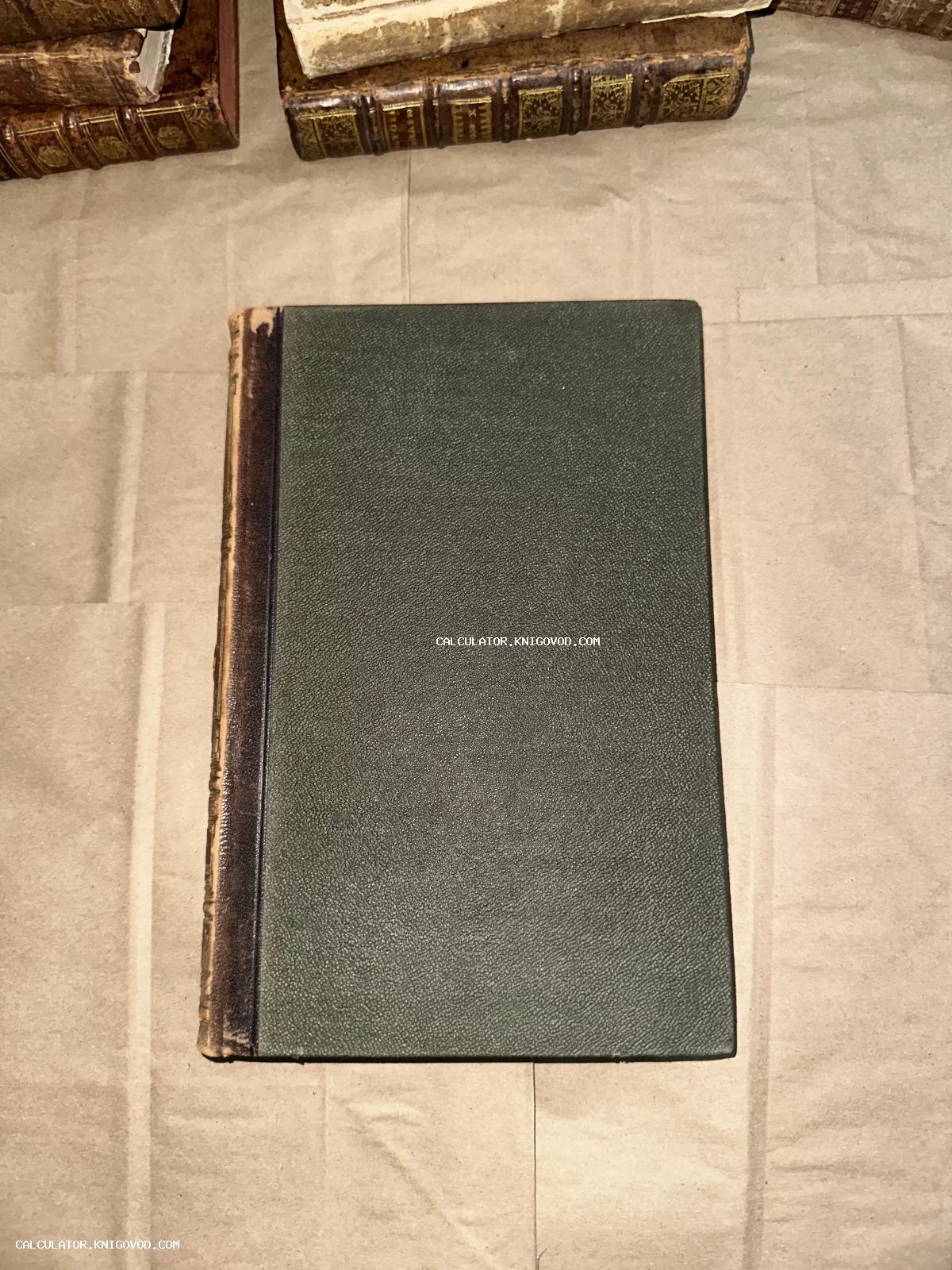 Вид сверху на антикварную книгу с темно-зеленой текстурированной обложкой и потертым кожаным корешком.