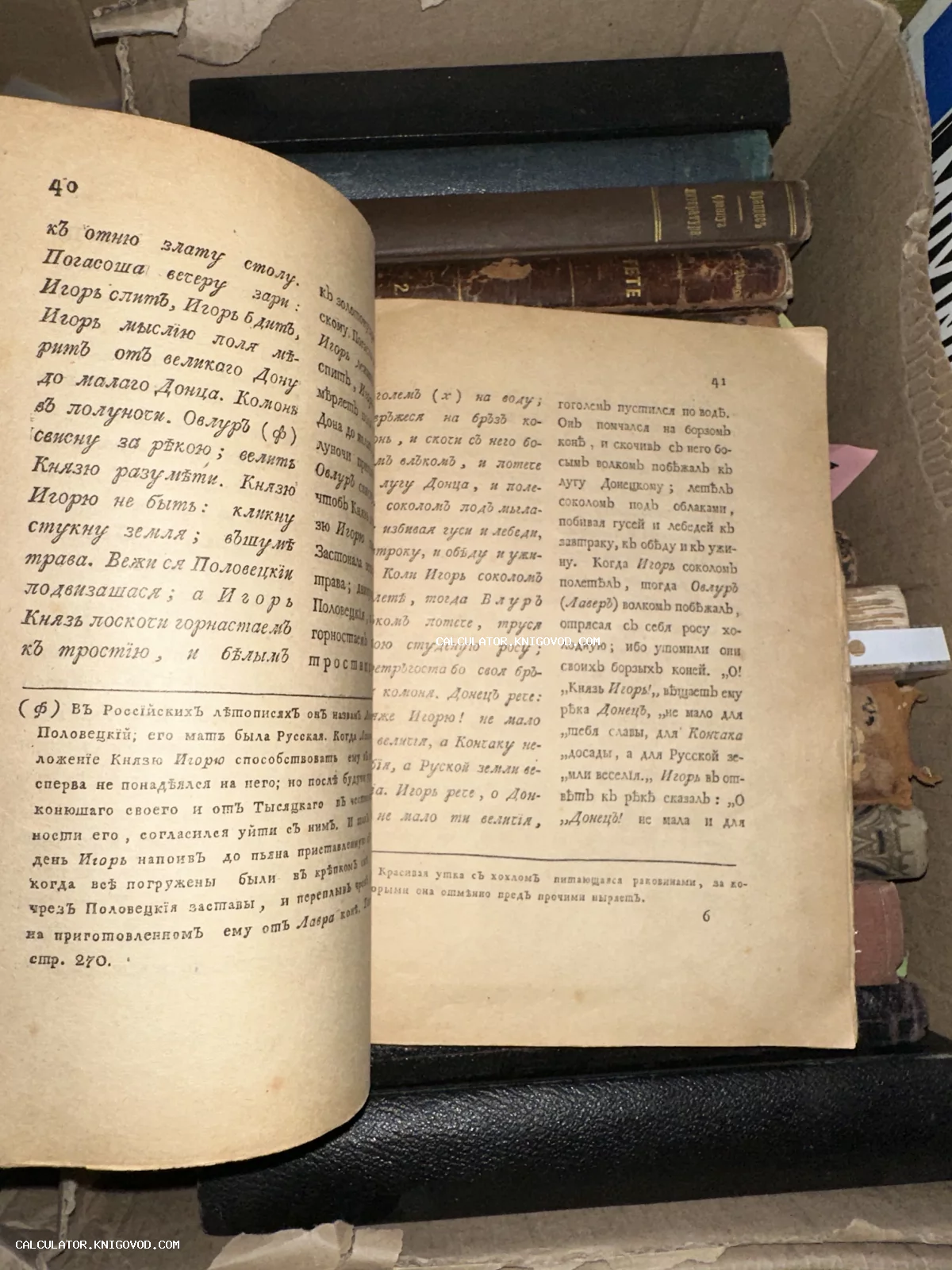 Разворот старинной книги с текстом на дореволюционном русском языке, лежащей в коробке среди других антикварных томов.