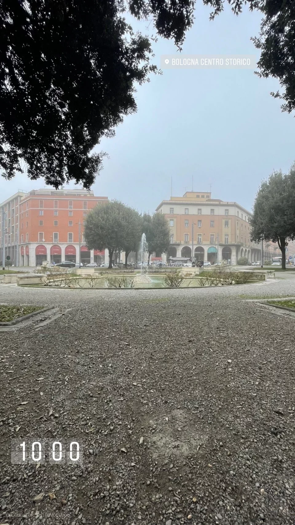 Вид на городскую площадь в Болонье с фонтаном, деревьями и классическими итальянскими зданиями в утренней дымке.