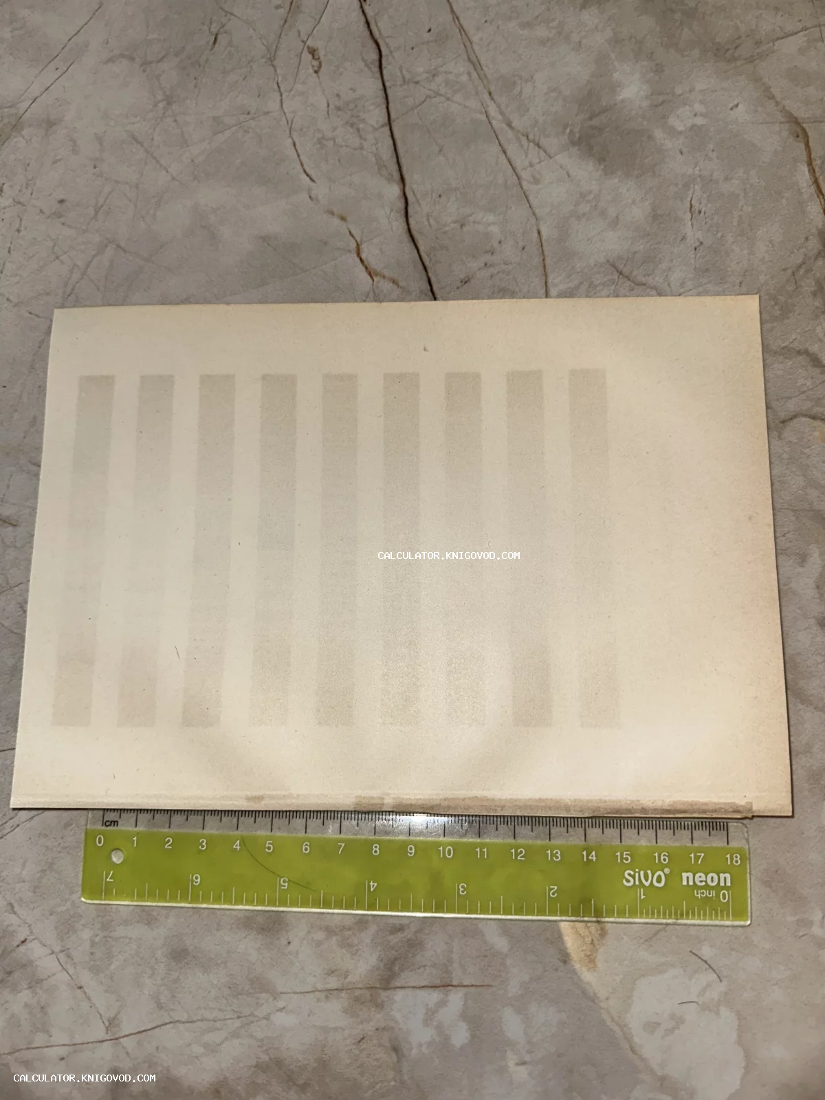 Оборотная сторона старинного бумажного листа рядом с измерительной линейкой, видна фактура бумаги и следы времени.