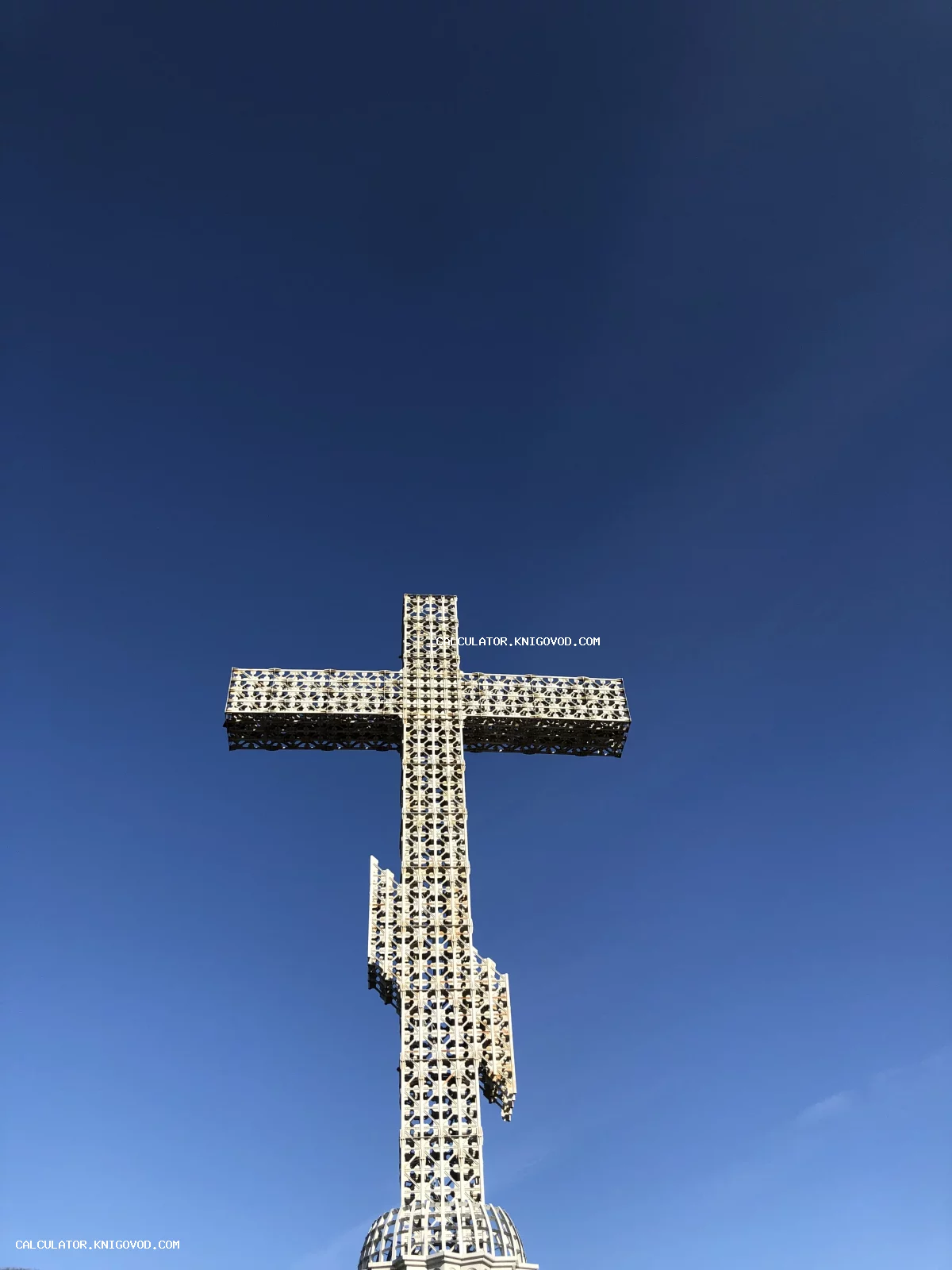 Большой металлический ажурный крест с орнаментом на фоне чистого ярко-синего неба.