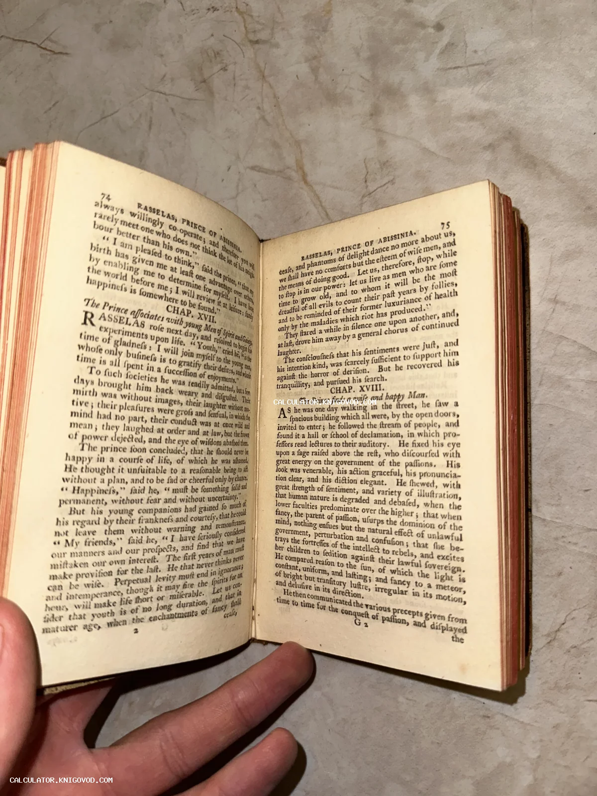 Разворот антикварной книги 'Rasselas, Prince of Abissinia' на английском языке с красным обрезом страниц в руке.