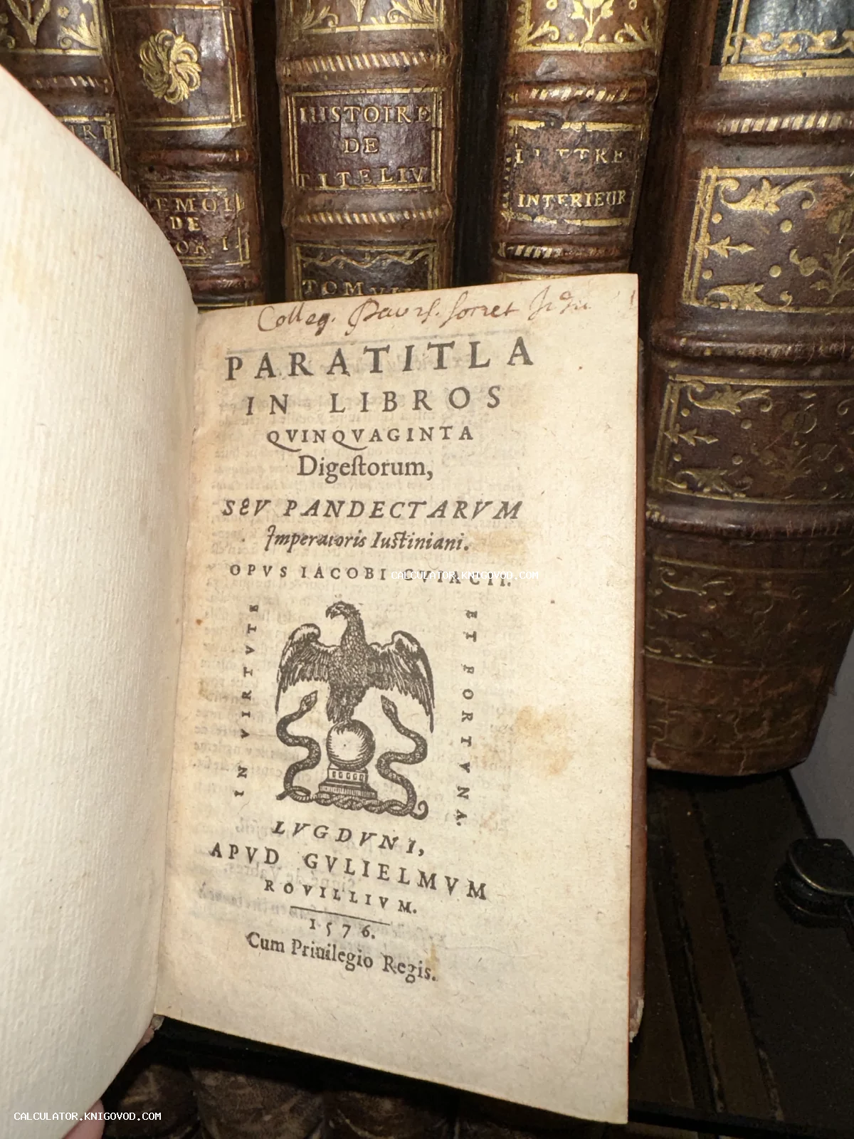 Титульный лист антикварной книги 1576 года издания на латыни с изображением орла, на заднем плане — старинные кожаные переплеты с золотым тиснением.