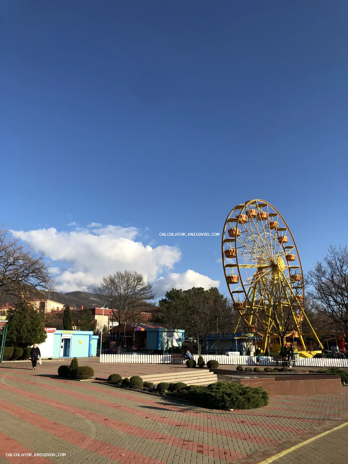 Желтое колесо обозрения в парке на фоне ярко-синего неба и далеких гор