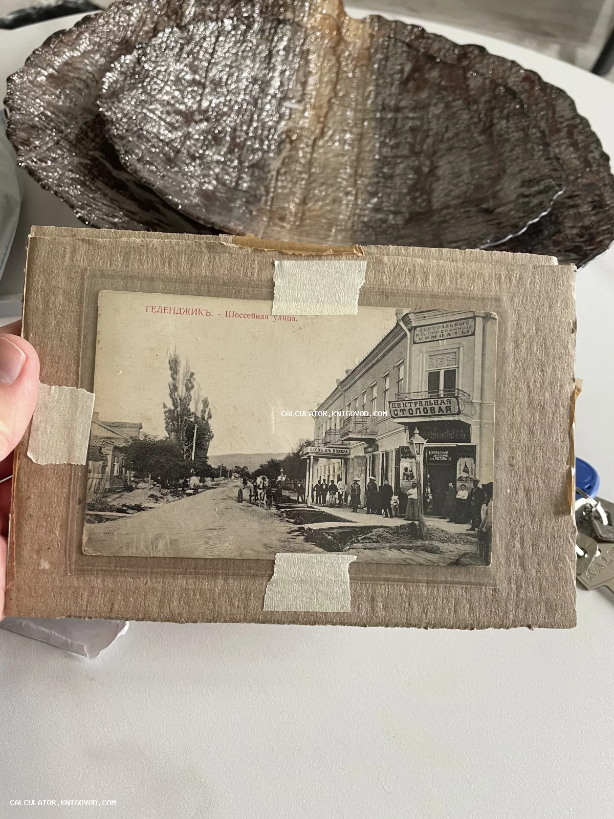 Черно-белая дореволюционная открытка с видом на Шоссейную улицу в Геленджике, запечатлевшая Центральную столовую и архитектуру начала XX века.