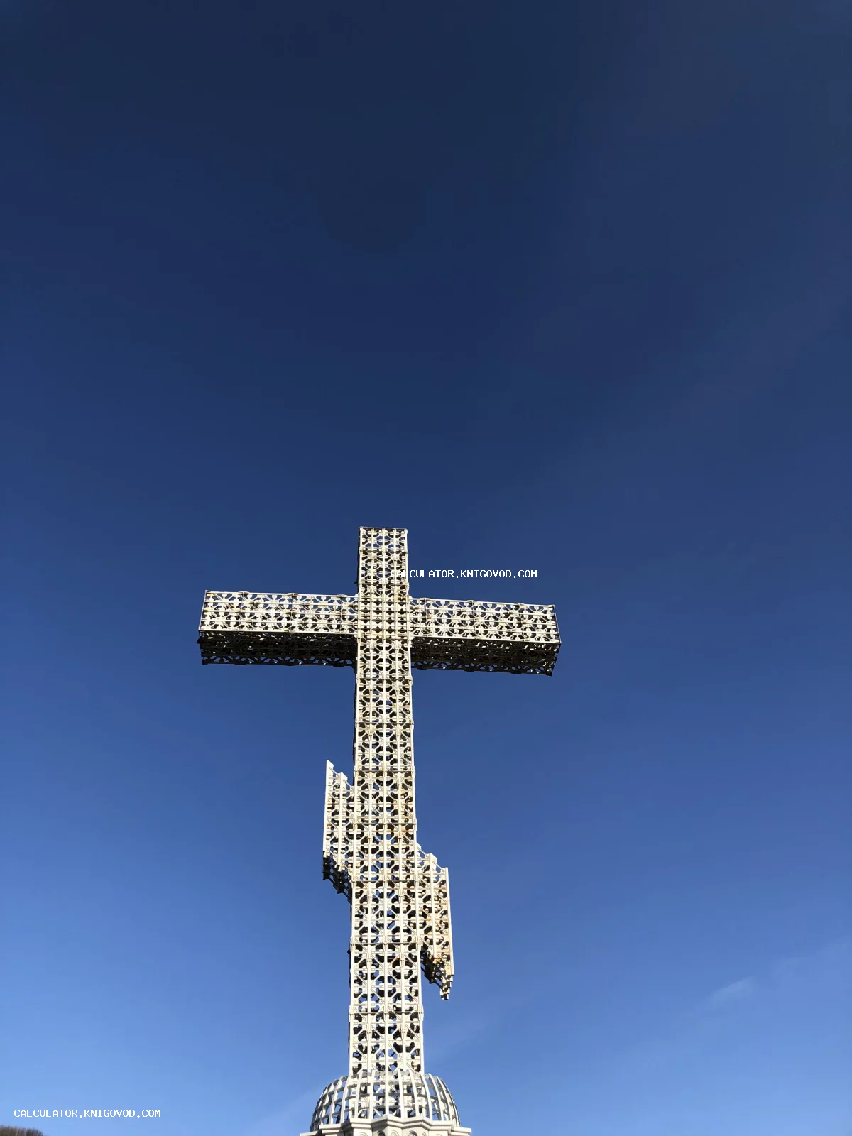 Массивный металлический православный крест с ажурным геометрическим узором на фоне чистого ярко-синего неба.