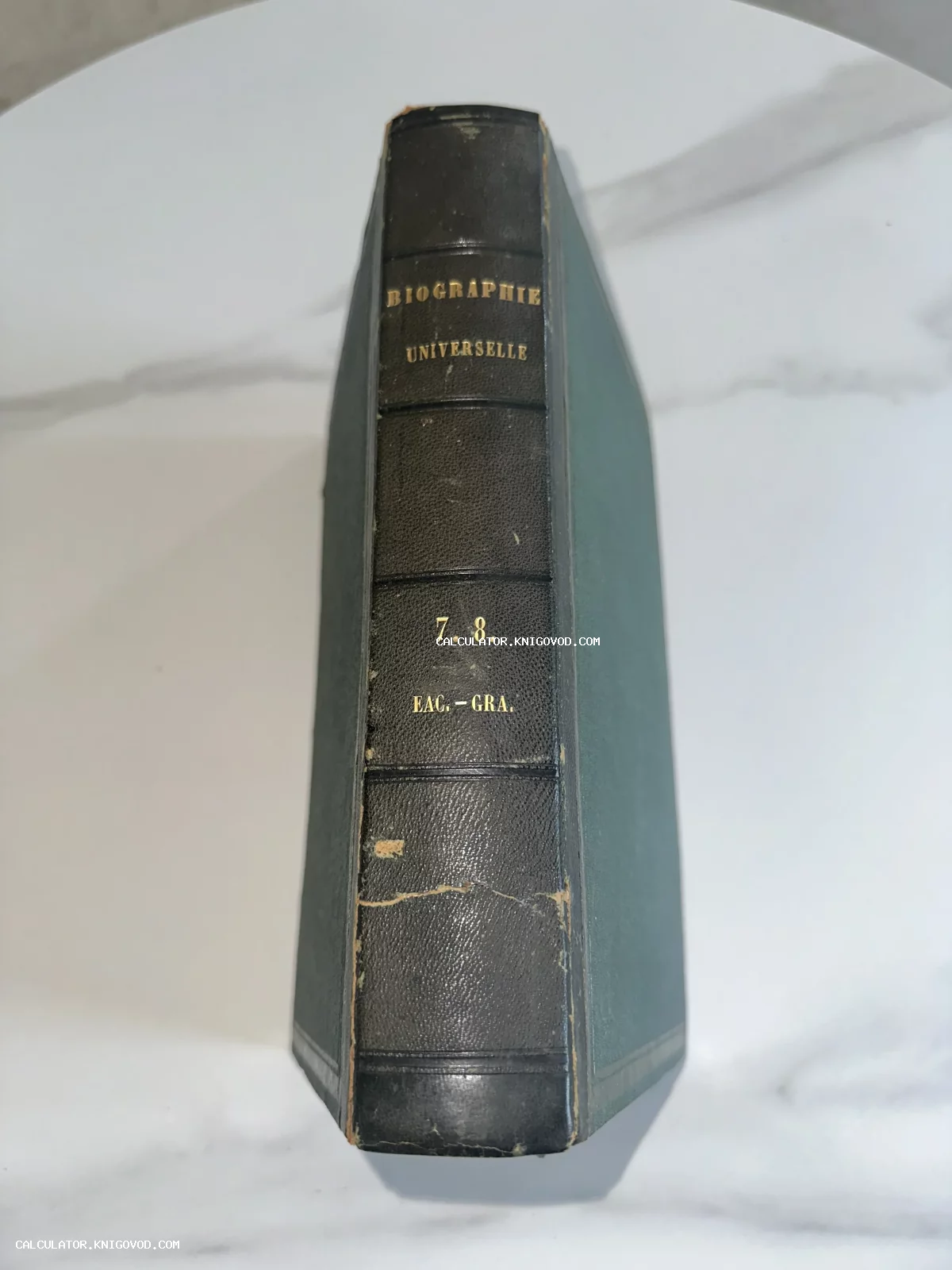 Корешок старинной книги Biographie Universelle в полукожаном переплете с золотым тиснением на фоне мраморной поверхности.