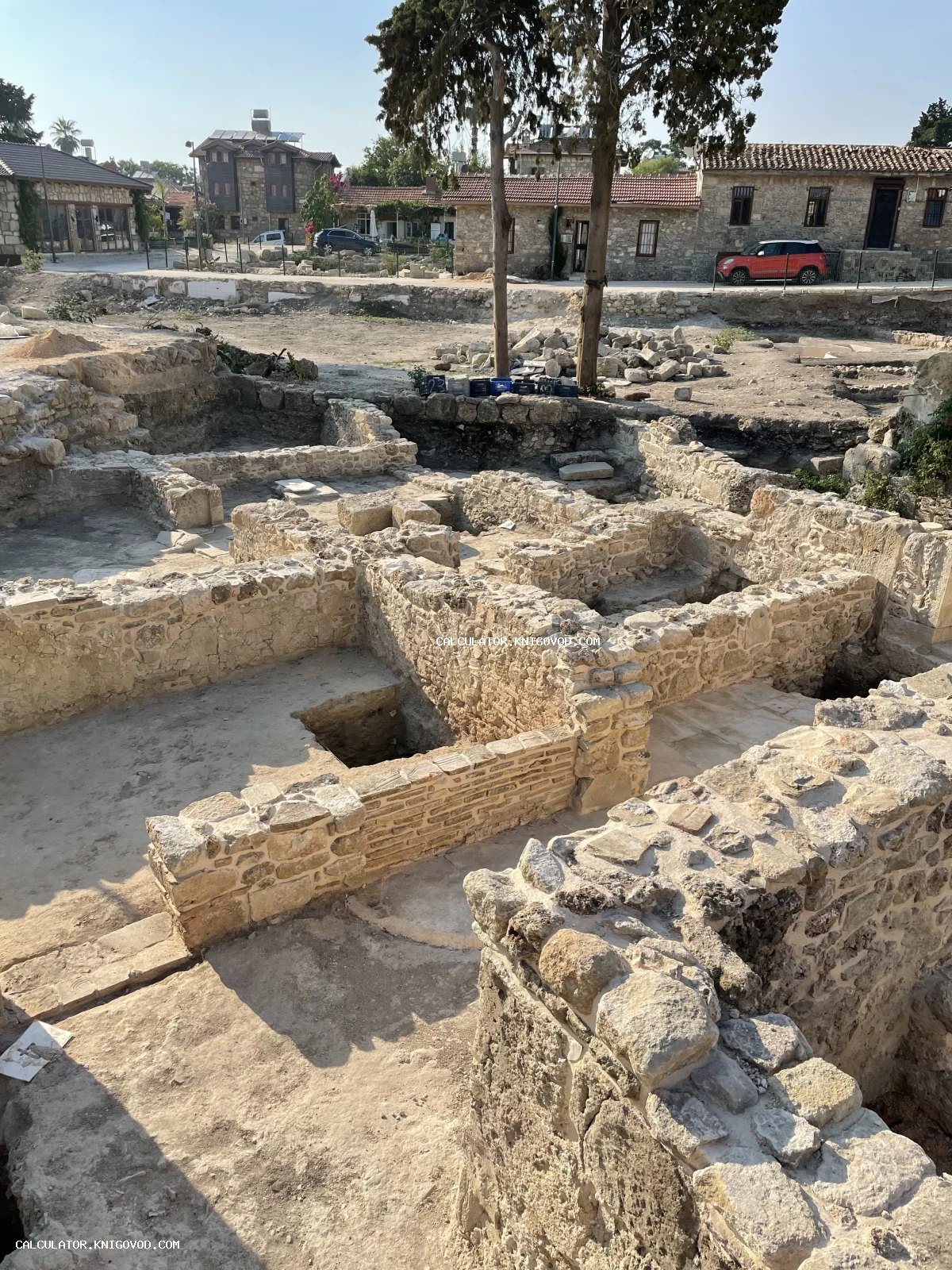 Вид сверху на каменные фундаменты и руины древних стен в месте археологических раскопок на фоне современных зданий.