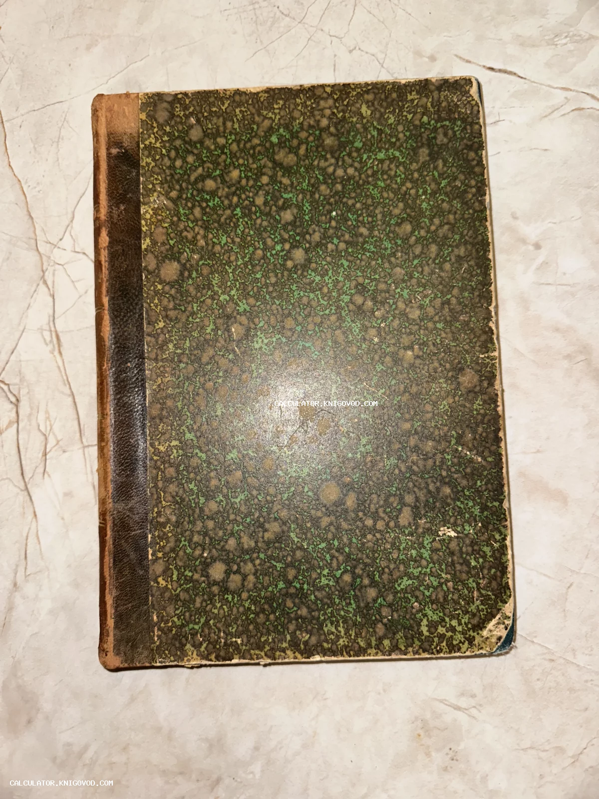 Вид сверху на обложку старинной антикварной книги с зеленым мраморным узором и потертым кожаным корешком