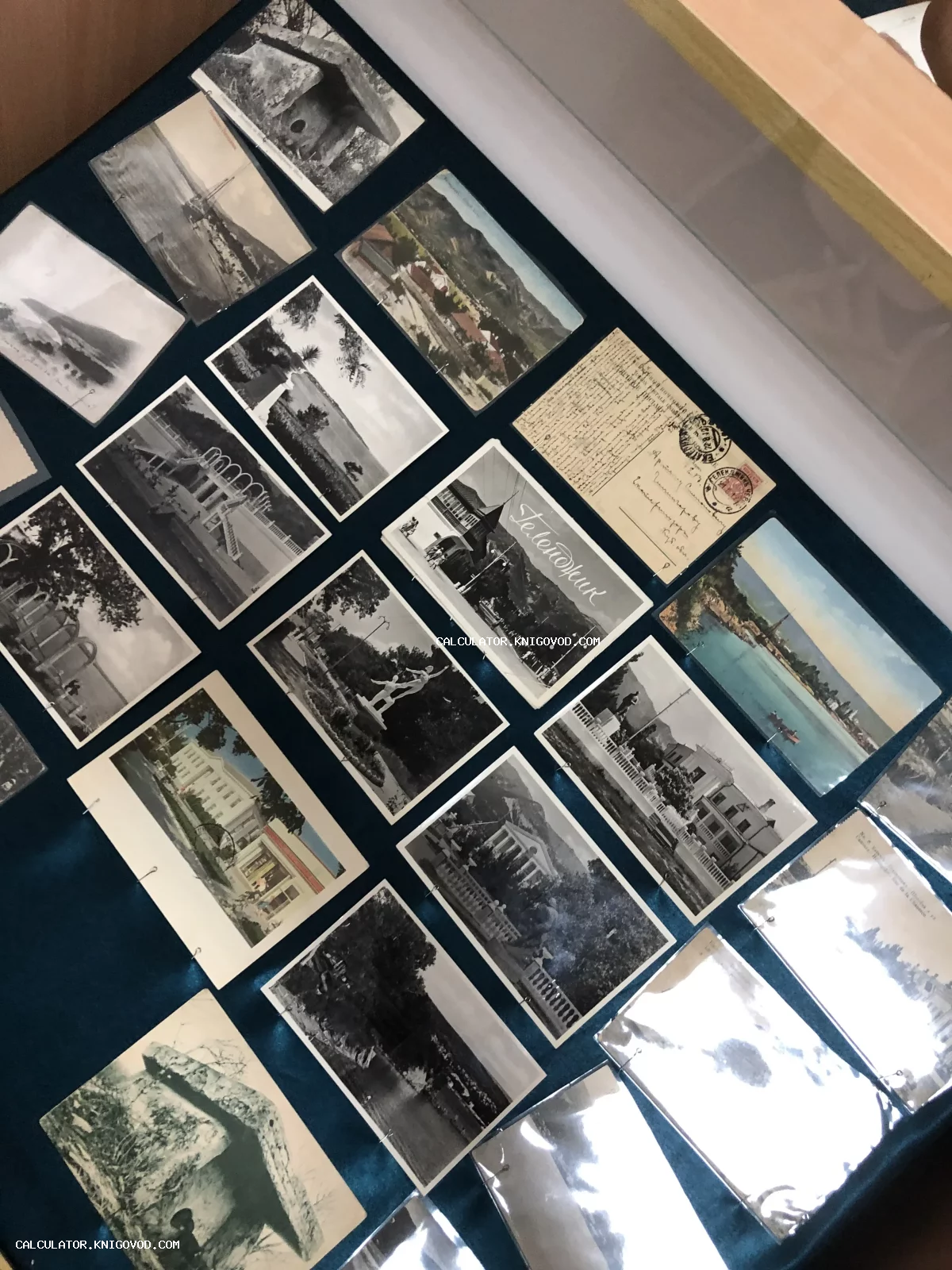 Собрание старинных черно-белых и цветных открыток с видами южных городов и дольменов, разложенных на синем бархате под стеклом.