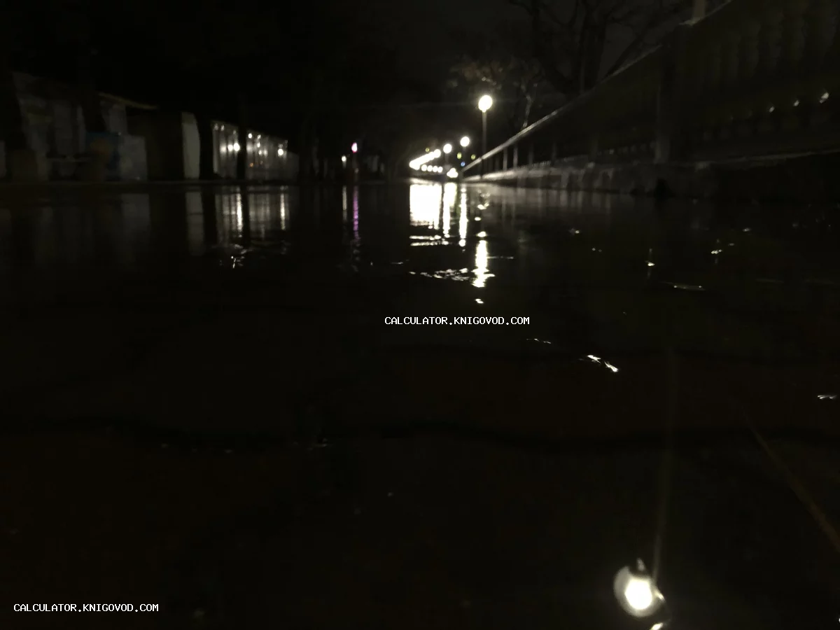 Отражение ярких уличных фонарей в лужах на мокром асфальте в темное время суток.