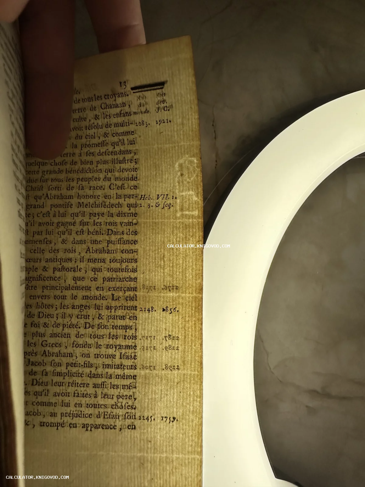 Крупный план страницы старинной книги на французском языке с видимой текстурой бумаги верже и водяным знаком под ярким светом.