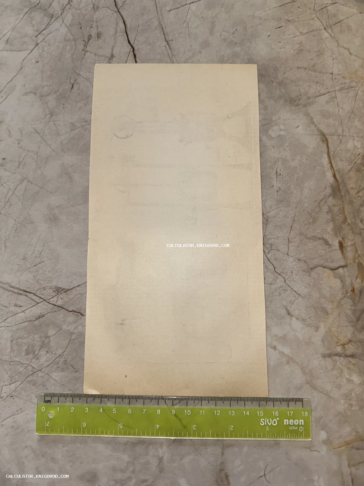 Обратная сторона старинного бумажного листа на мраморной поверхности рядом с зеленой линейкой.